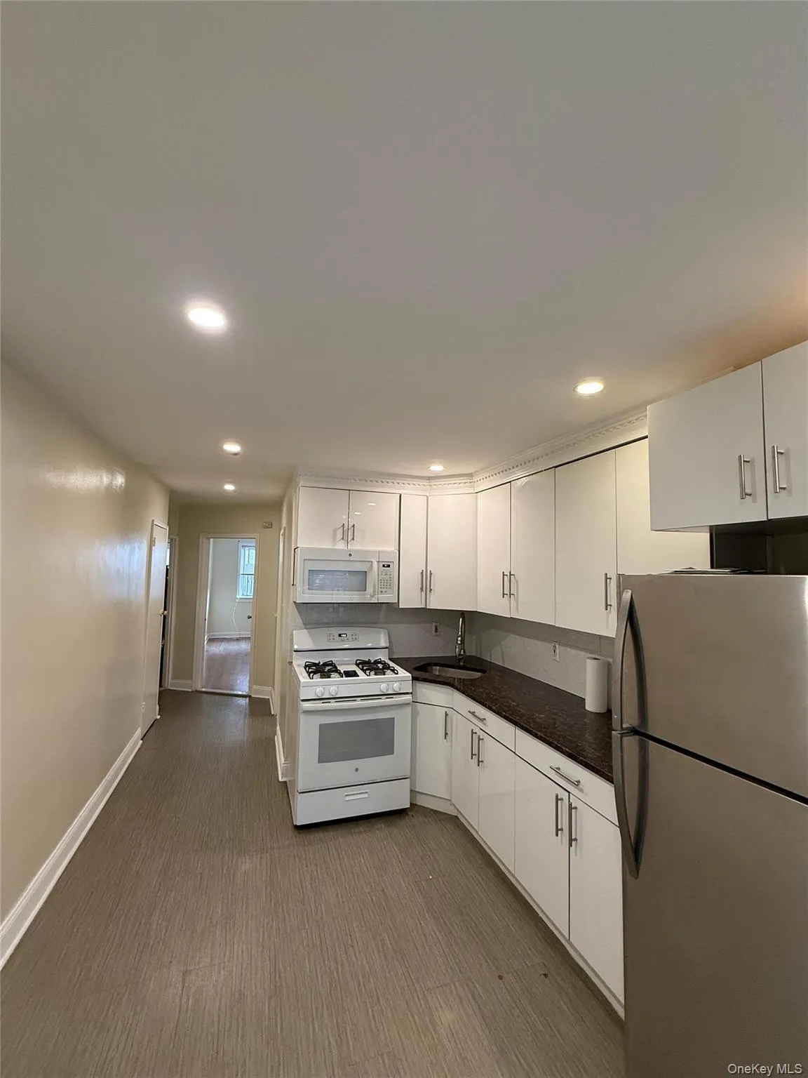Kitchen with white appliances, recessed lighting, white cabinetry, and dark wood-style floors Kitchen with white appliances, recessed lighting, white cabinetry, and dark wood-style floors