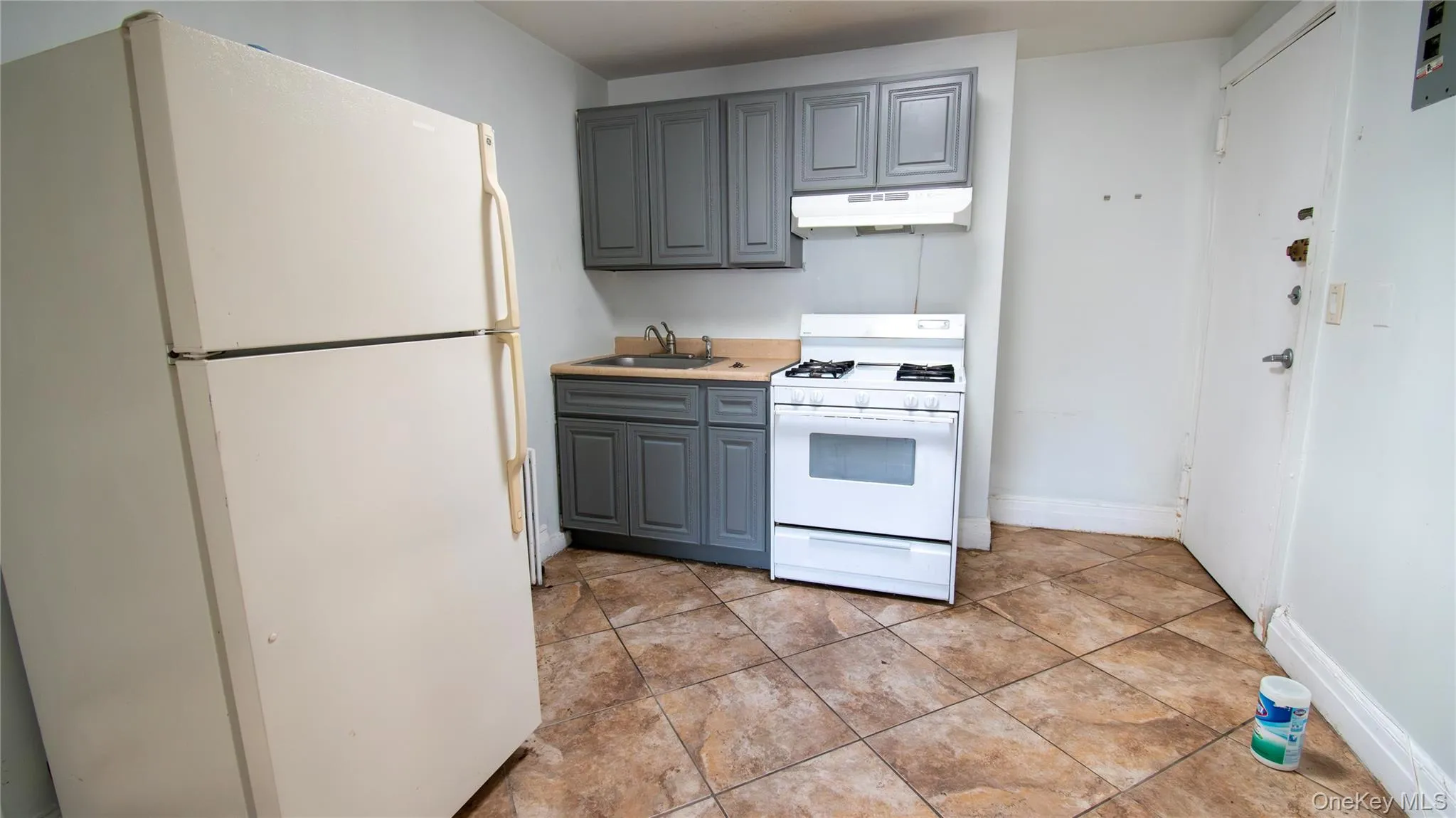 Kitchen with white appliances, gray cabinets, light countertops, under cabinet range hood, and light tile patterned floors Kitchen with white appliances, gray cabinets, light countertops, under cabinet range hood, and light tile patterned floors