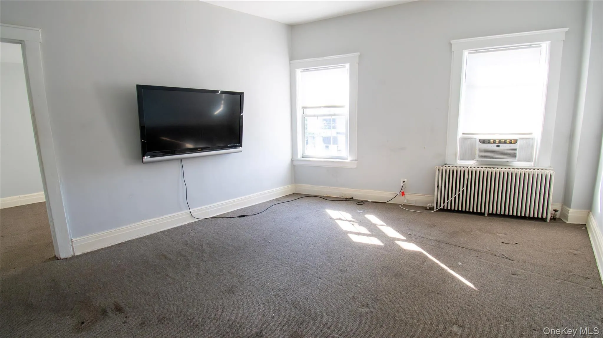 Unfurnished living room featuring radiator, carpet flooring, and cooling unit Unfurnished living room featuring radiator, carpet flooring, and cooling unit