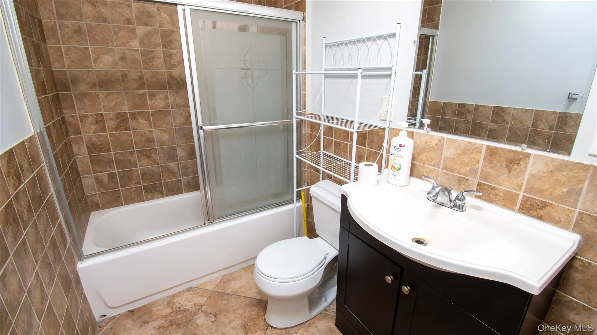 Bathroom featuring tile walls, combined bath / shower with glass door, vanity, and decorative backsplash Bathroom featuring tile walls, combined bath / shower with glass door, vanity, and decorative backsplash