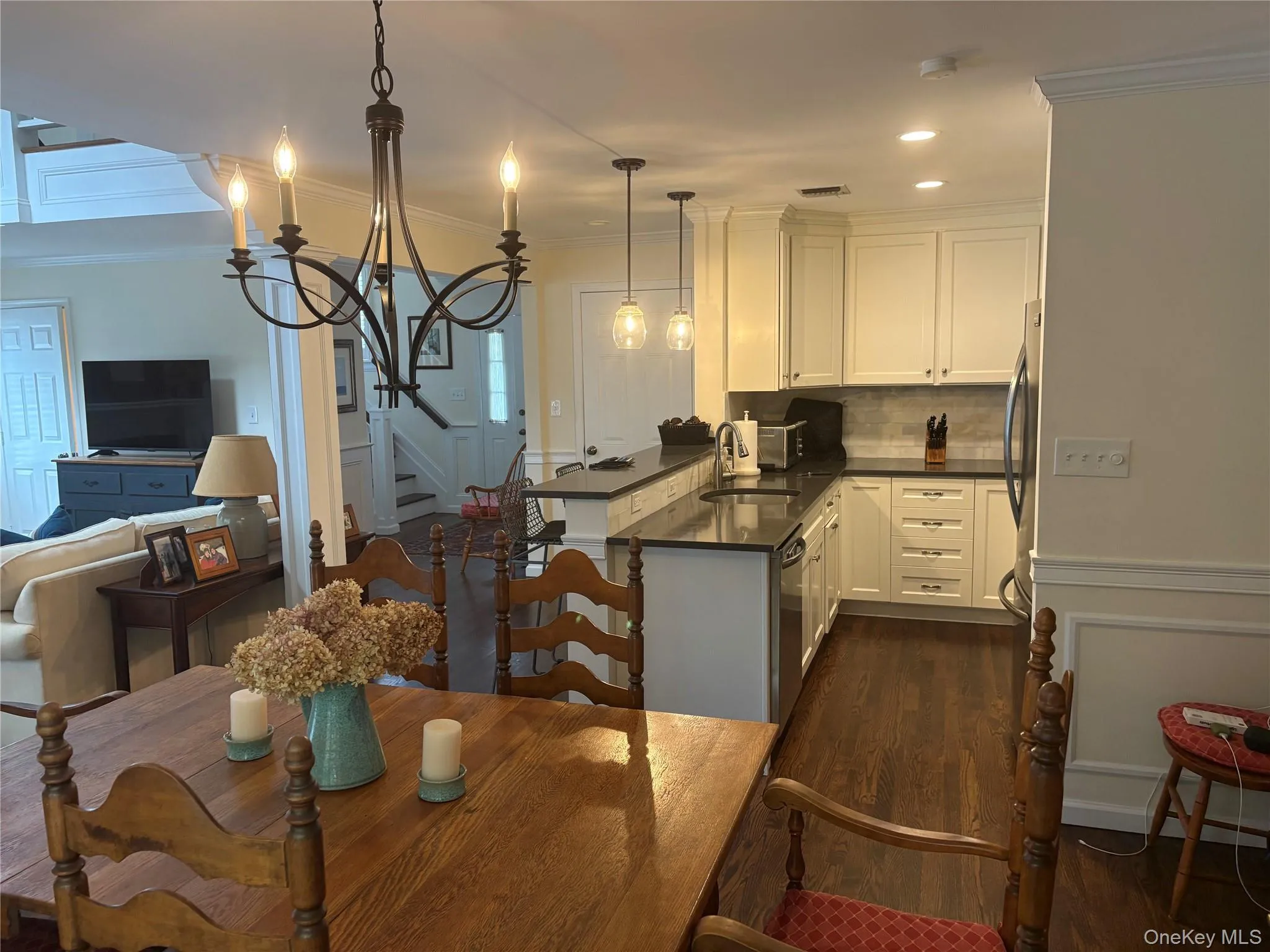 Kitchen featuring ornamental molding, center island, hanging fixtures and white cabinets and adjacent dining area with chandelier Kitchen featuring ornamental molding, center island, hanging fixtures and white cabinets and adjacent dining area with chandelier