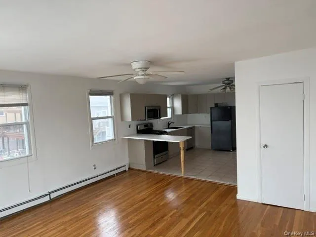 Kitchen with a baseboard heating unit, appliances with stainless steel finishes, light countertops, a peninsula, and light wood finished floors Kitchen with a baseboard heating unit, appliances with stainless steel finishes, light countertops, a peninsula, and light wood finished floors
