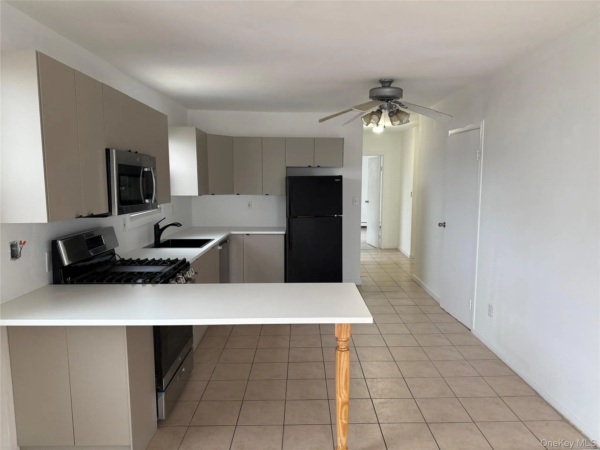 Kitchen with appliances with stainless steel finishes, light countertops, light tile patterned flooring, a peninsula, and ceiling fan Kitchen with appliances with stainless steel finishes, light countertops, light tile patterned flooring, a peninsula, and ceiling fan