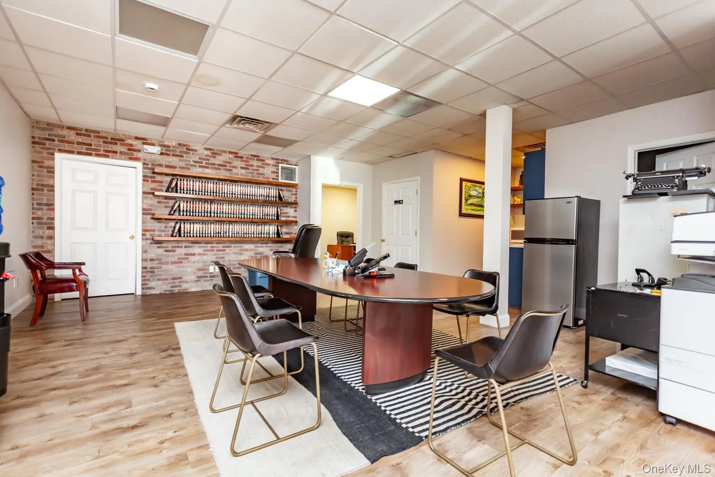 Home office with brick wall, light wood-style flooring, and a drop ceiling Home office with brick wall, light wood-style flooring, and a drop ceiling