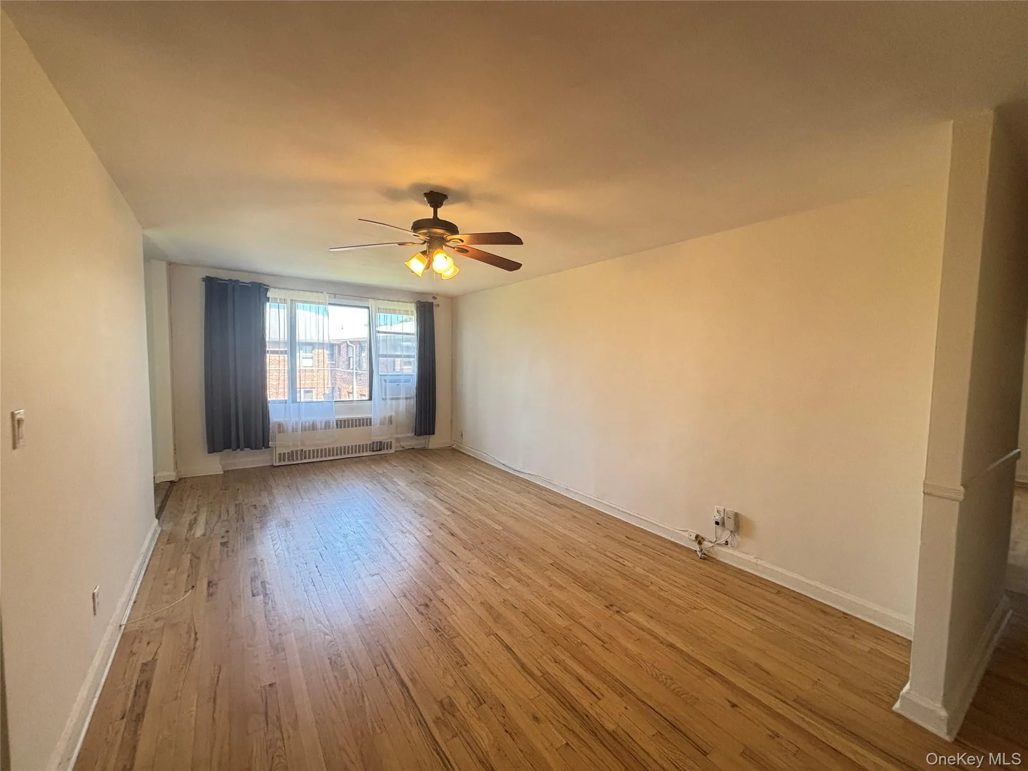 Unfurnished room with light wood-style floors, a ceiling fan, and radiator heating unit Unfurnished room with light wood-style floors, a ceiling fan, and radiator heating unit