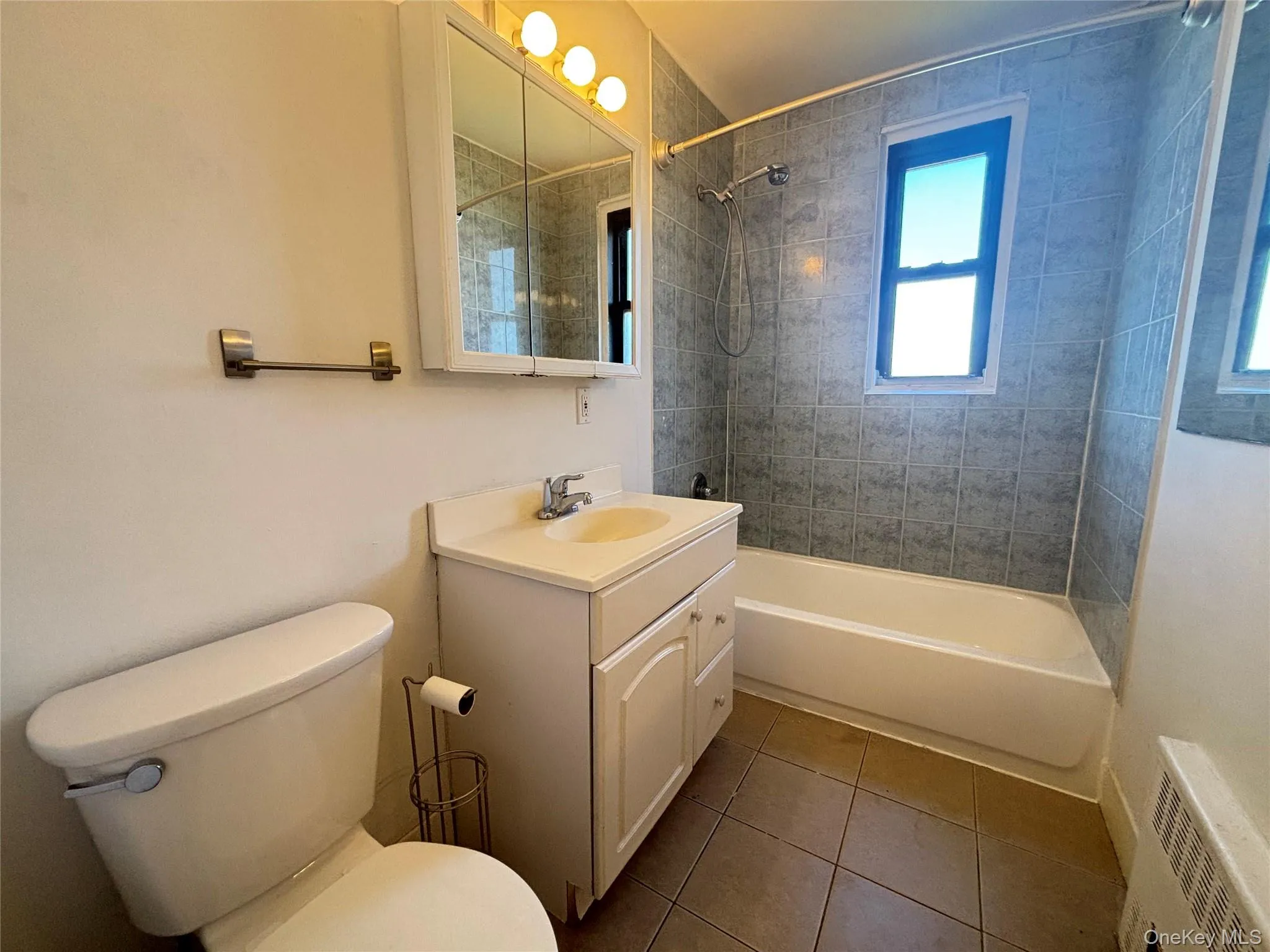 Bathroom with bathtub / shower combination, vanity, and dark tile patterned floors Bathroom with bathtub / shower combination, vanity, and dark tile patterned floors