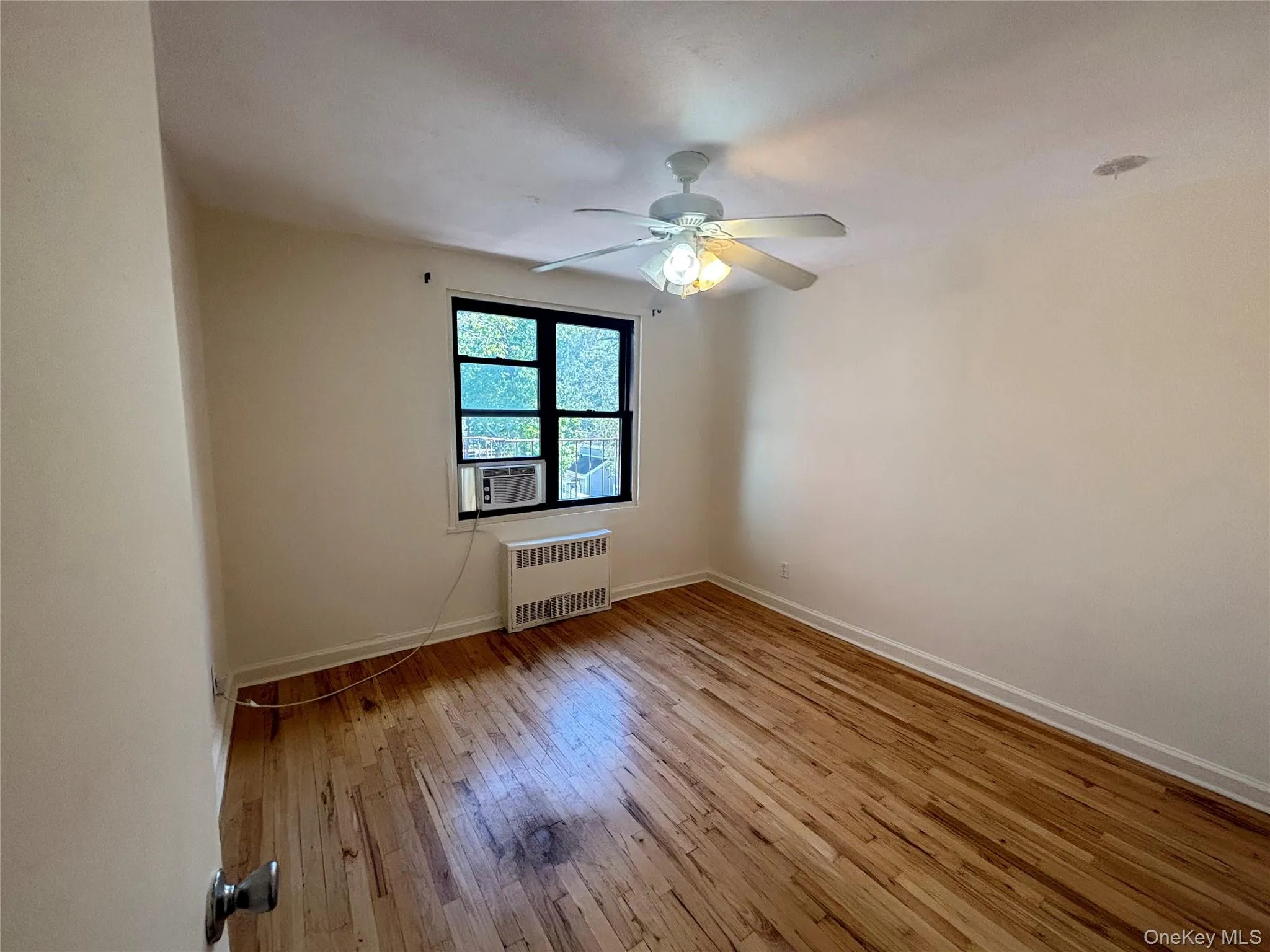 Unfurnished room with light wood-type flooring, a ceiling fan, and radiator Unfurnished room with light wood-type flooring, a ceiling fan, and radiator