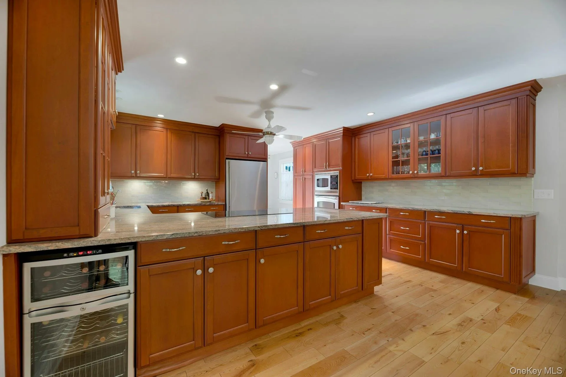 Kitchen with light stone counters, a peninsula, wine cooler, tasteful backsplash, and stainless steel appliances Kitchen with light stone counters, a peninsula, wine cooler, tasteful backsplash, and stainless steel appliances