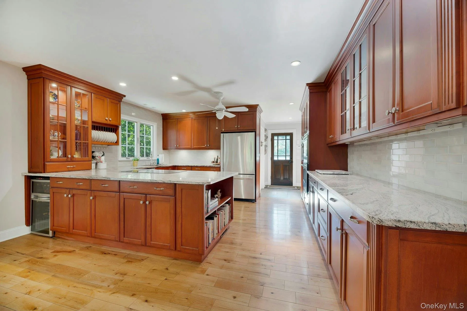 Kitchen with glass insert cabinets, brown cabinets, a peninsula, light stone countertops, and recessed lighting Kitchen with glass insert cabinets, brown cabinets, a peninsula, light stone countertops, and recessed lighting