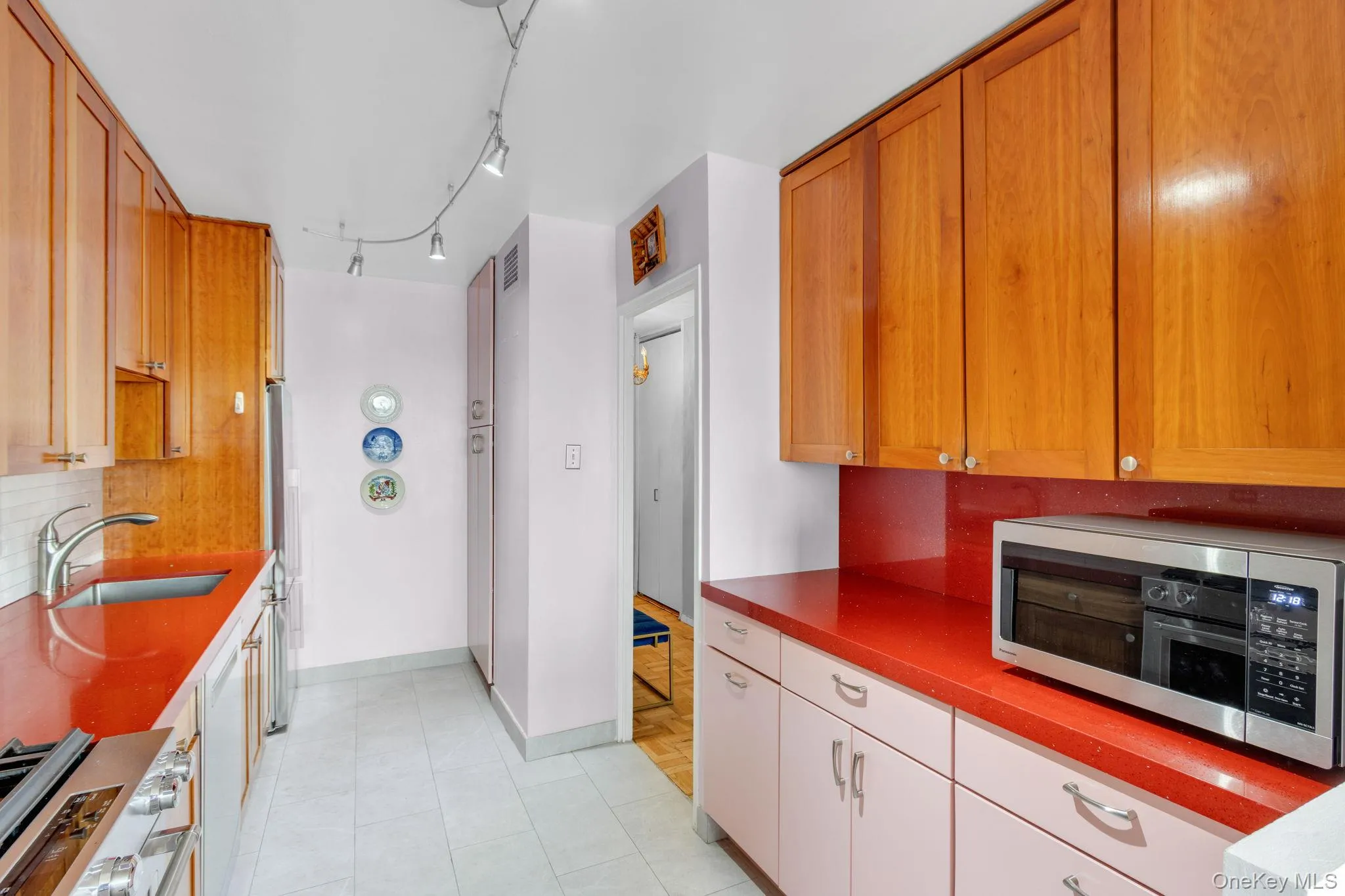Kitchen with stainless steel appliances, decorative backsplash, light tile patterned floors, dark countertops, and brown cabinets Kitchen with stainless steel appliances, decorative backsplash, light tile patterned floors, dark countertops, and brown cabinets