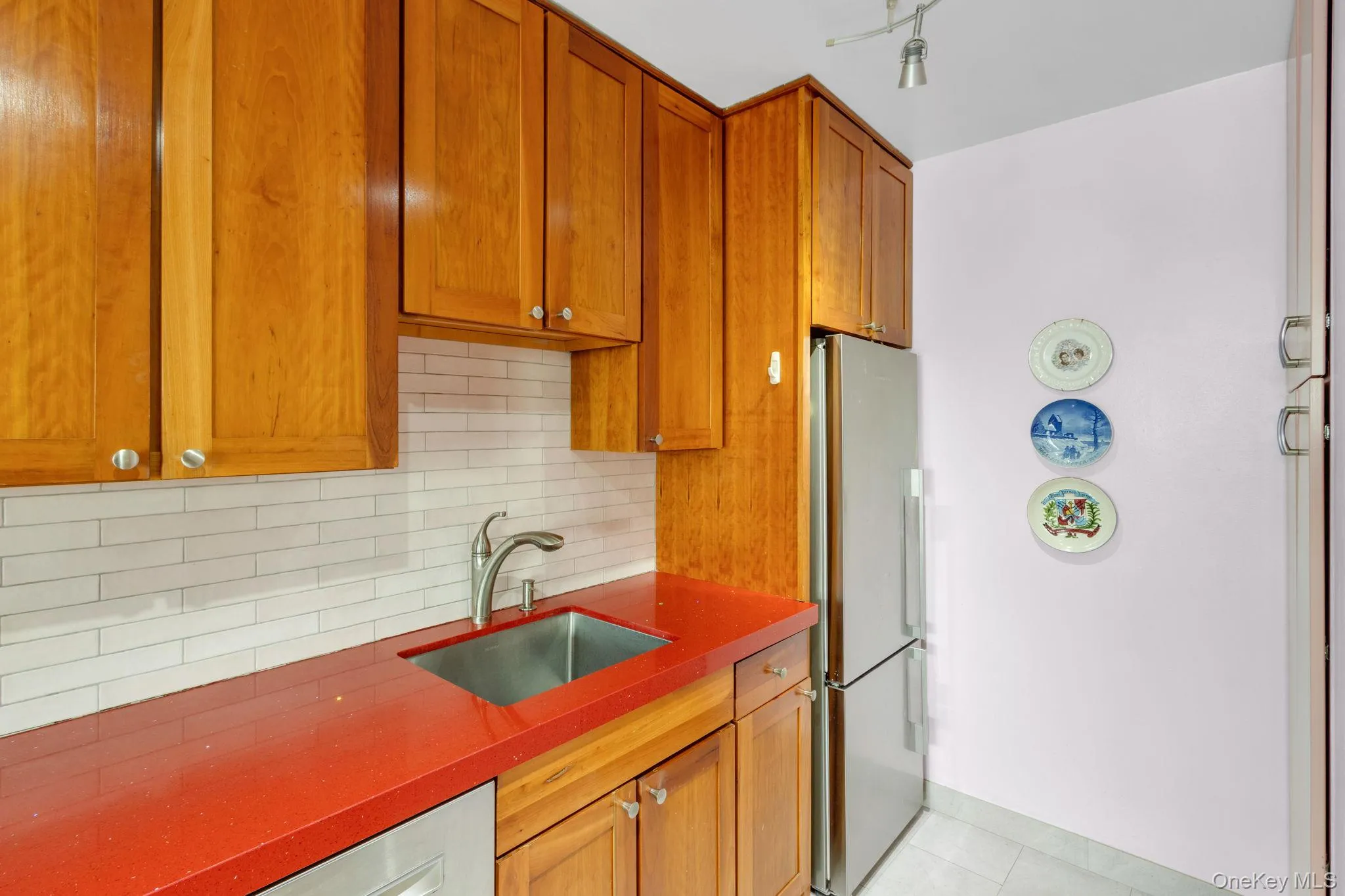 Kitchen featuring backsplash, brown cabinetry, freestanding refrigerator, light tile patterned flooring, and dark stone counters Kitchen featuring backsplash, brown cabinetry, freestanding refrigerator, light tile patterned flooring, and dark stone counters