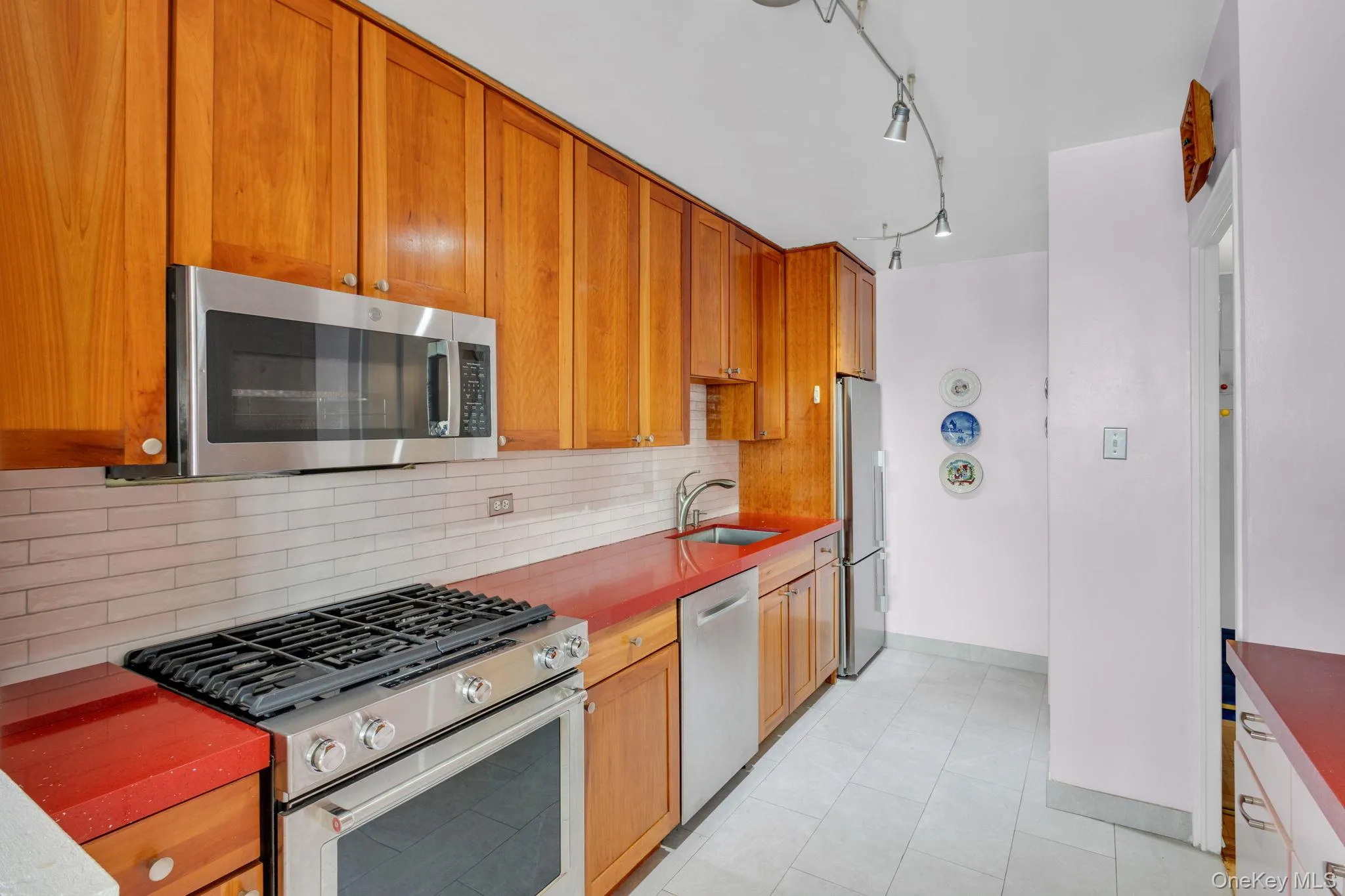 Kitchen featuring appliances with stainless steel finishes, backsplash, brown cabinets, light tile patterned flooring, and dark countertops Kitchen featuring appliances with stainless steel finishes, backsplash, brown cabinets, light tile patterned flooring, and dark countertops