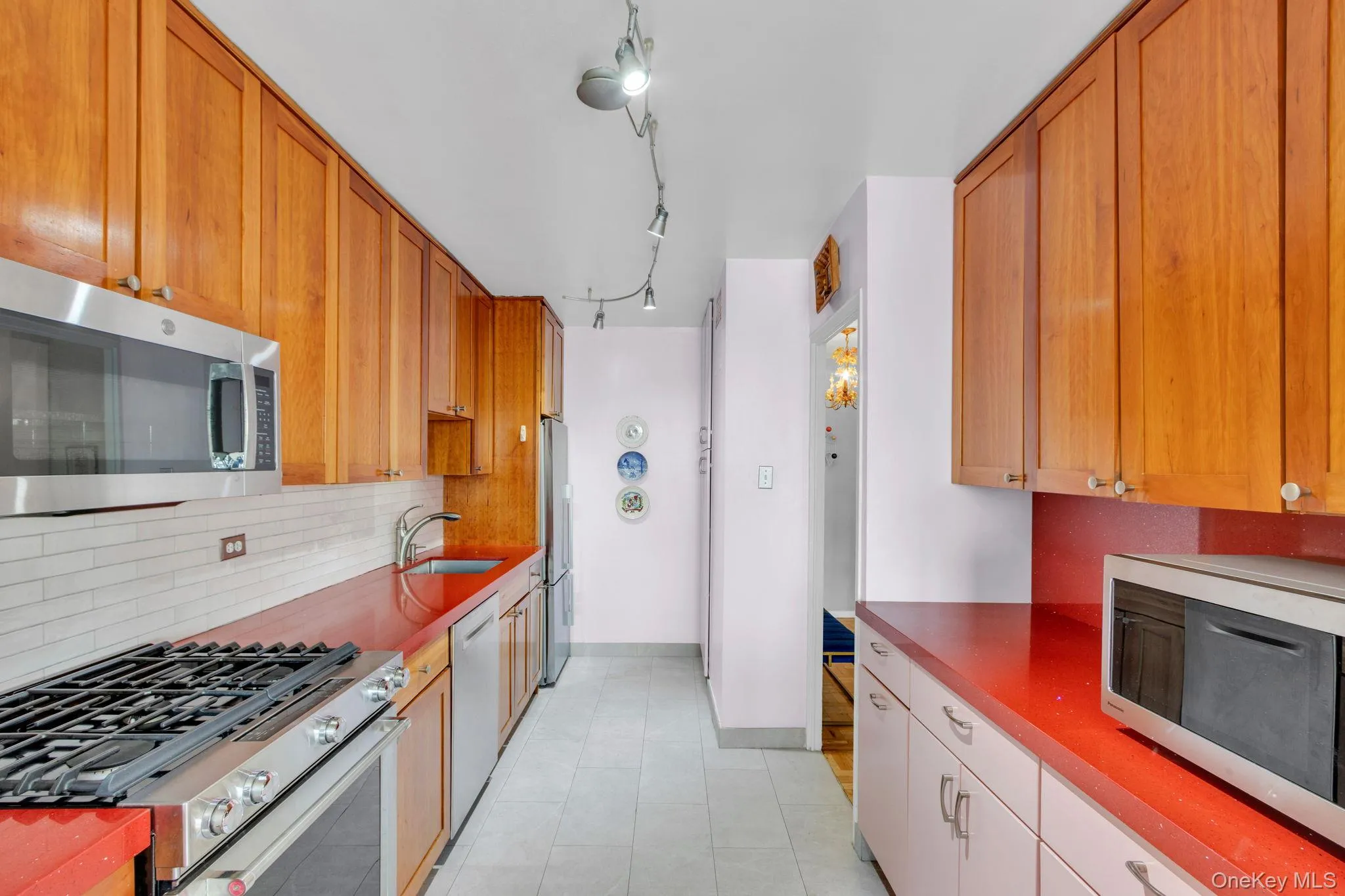 Kitchen featuring appliances with stainless steel finishes, tasteful backsplash, track lighting, light tile patterned floors, and dark countertops Kitchen featuring appliances with stainless steel finishes, tasteful backsplash, track lighting, light tile patterned floors, and dark countertops