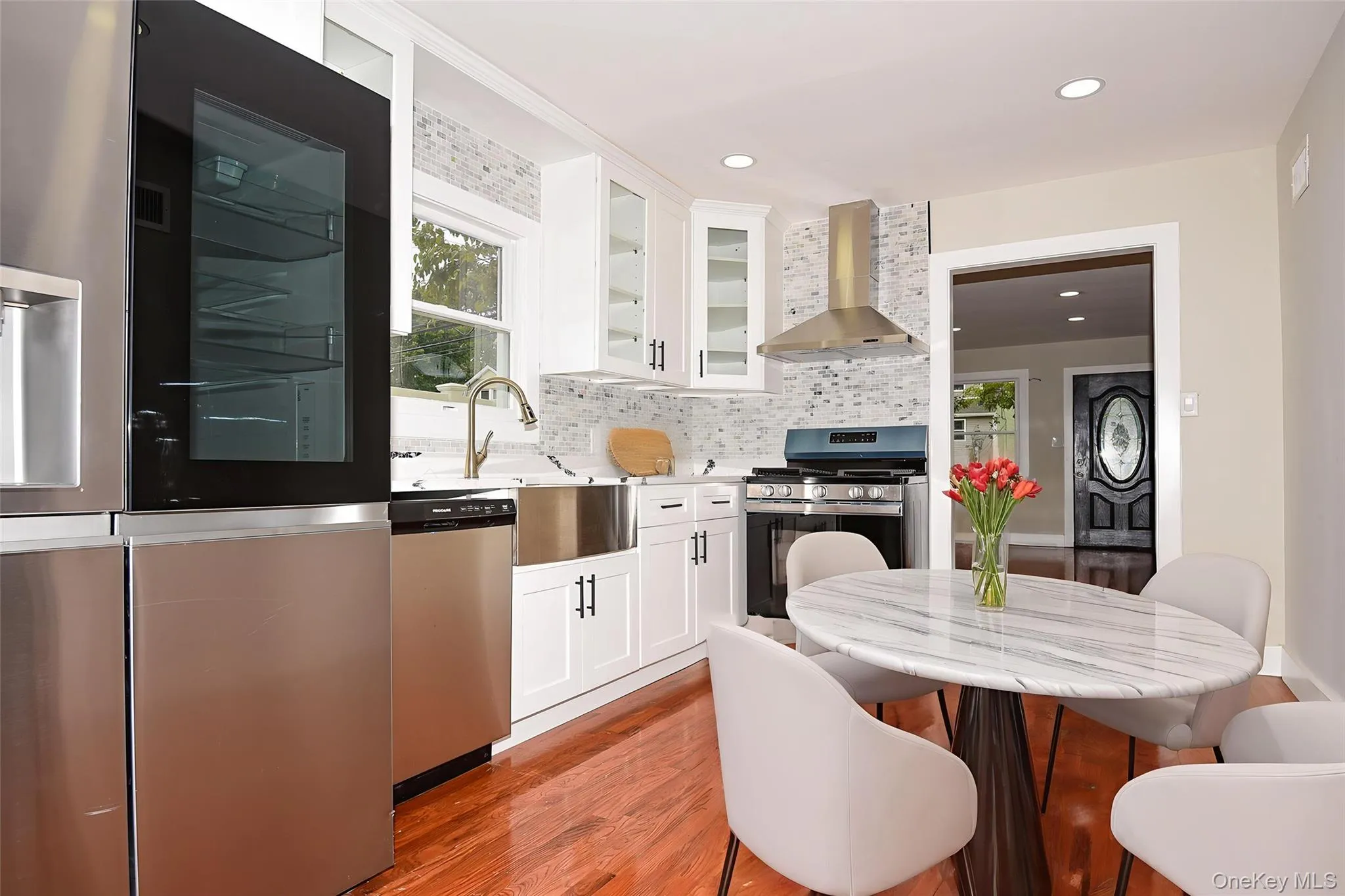 Kitchen featuring white cabinetry, appliances with stainless steel finishes, wall chimney range hood, light wood-style floors, and decorative backsplash Kitchen featuring white cabinetry, appliances with stainless steel finishes, wall chimney range hood, light wood-style floors, and decorative backsplash