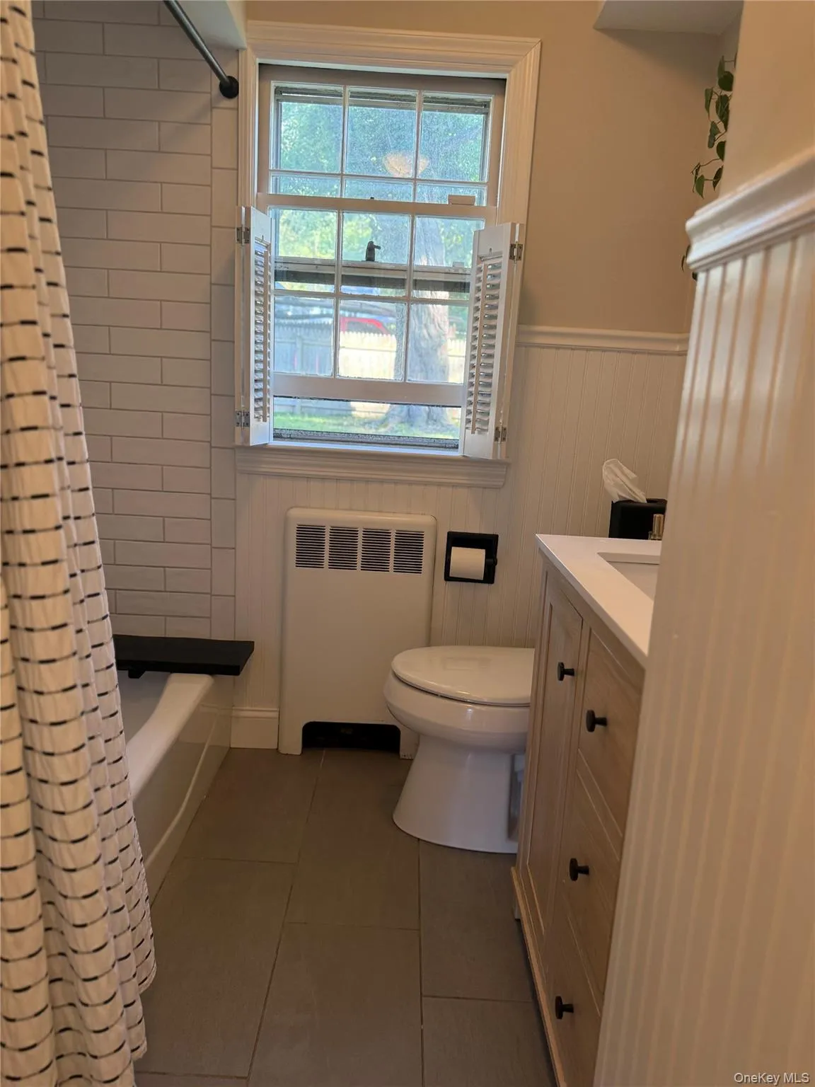 Bathroom featuring radiator, vanity, dark tile patterned flooring, shower / bath combo with shower curtain, and a wainscoted wall Bathroom featuring radiator, vanity, dark tile patterned flooring, shower / bath combo with shower curtain, and a wainscoted wall