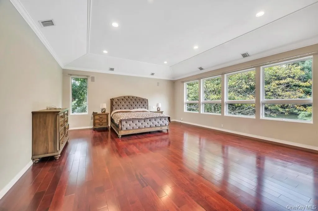 Bedroom with dark wood-style flooring, crown molding, a raised ceiling, and recessed lighting Bedroom with dark wood-style flooring, crown molding, a raised ceiling, and recessed lighting