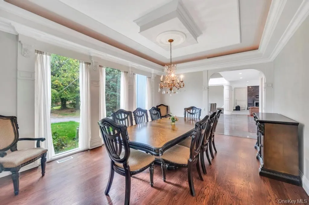 Dining space with a tray ceiling, arched walkways, dark wood-type flooring, a chandelier, and ornamental molding Dining space with a tray ceiling, arched walkways, dark wood-type flooring, a chandelier, and ornamental molding