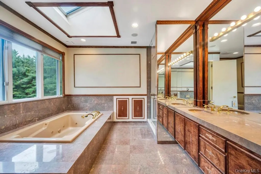 Full bathroom featuring a tub with jets, double vanity, a skylight, recessed lighting, and ornamental molding Full bathroom featuring a tub with jets, double vanity, a skylight, recessed lighting, and ornamental molding