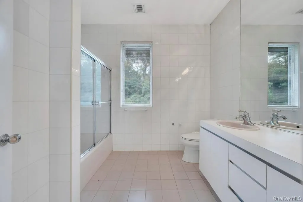 Full bathroom featuring tile walls, light tile patterned floors, bath / shower combo with glass door, and vanity Full bathroom featuring tile walls, light tile patterned floors, bath / shower combo with glass door, and vanity