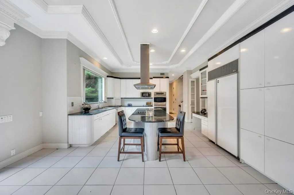 Kitchen featuring a kitchen breakfast bar, white cabinetry, appliances with stainless steel finishes, a center island, and island range hood Kitchen featuring a kitchen breakfast bar, white cabinetry, appliances with stainless steel finishes, a center island, and island range hood