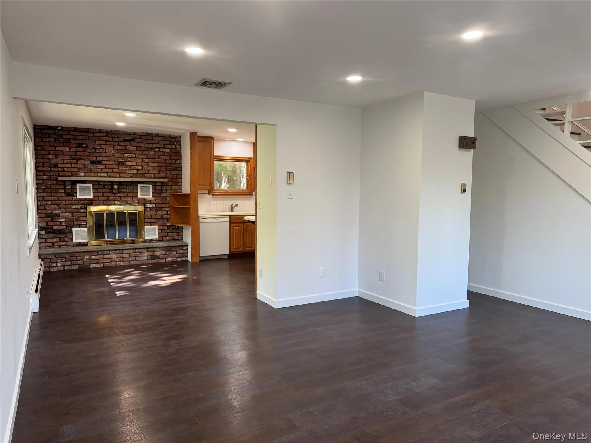 Unfurnished living room featuring recessed lighting, a brick fireplace, dark wood-type flooring, stairs, and baseboard heating Unfurnished living room featuring recessed lighting, a brick fireplace, dark wood-type flooring, stairs, and baseboard heating