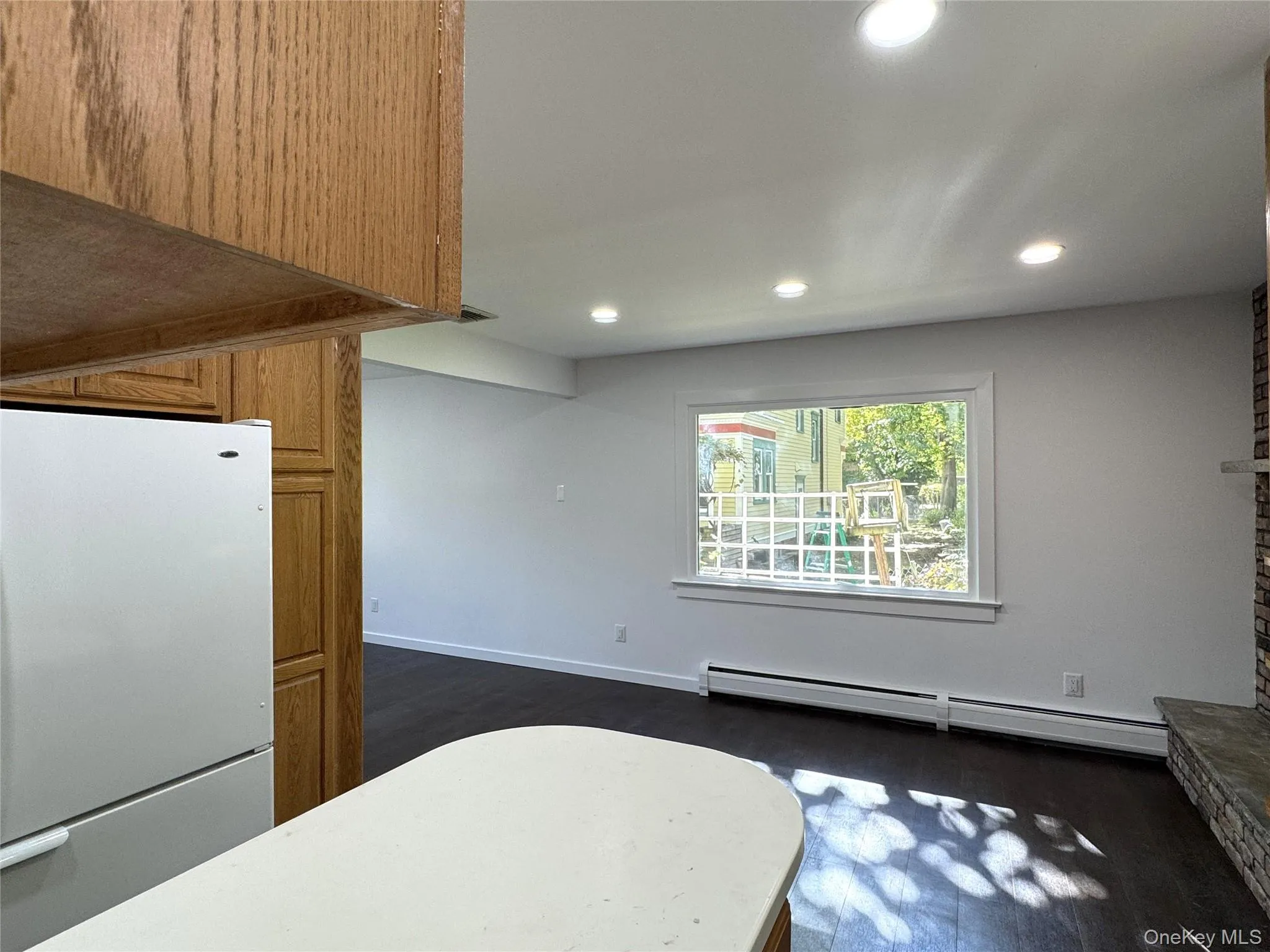 Kitchen with freestanding refrigerator, baseboard heating, dark wood-style flooring, recessed lighting, and brown cabinetry Kitchen with freestanding refrigerator, baseboard heating, dark wood-style flooring, recessed lighting, and brown cabinetry