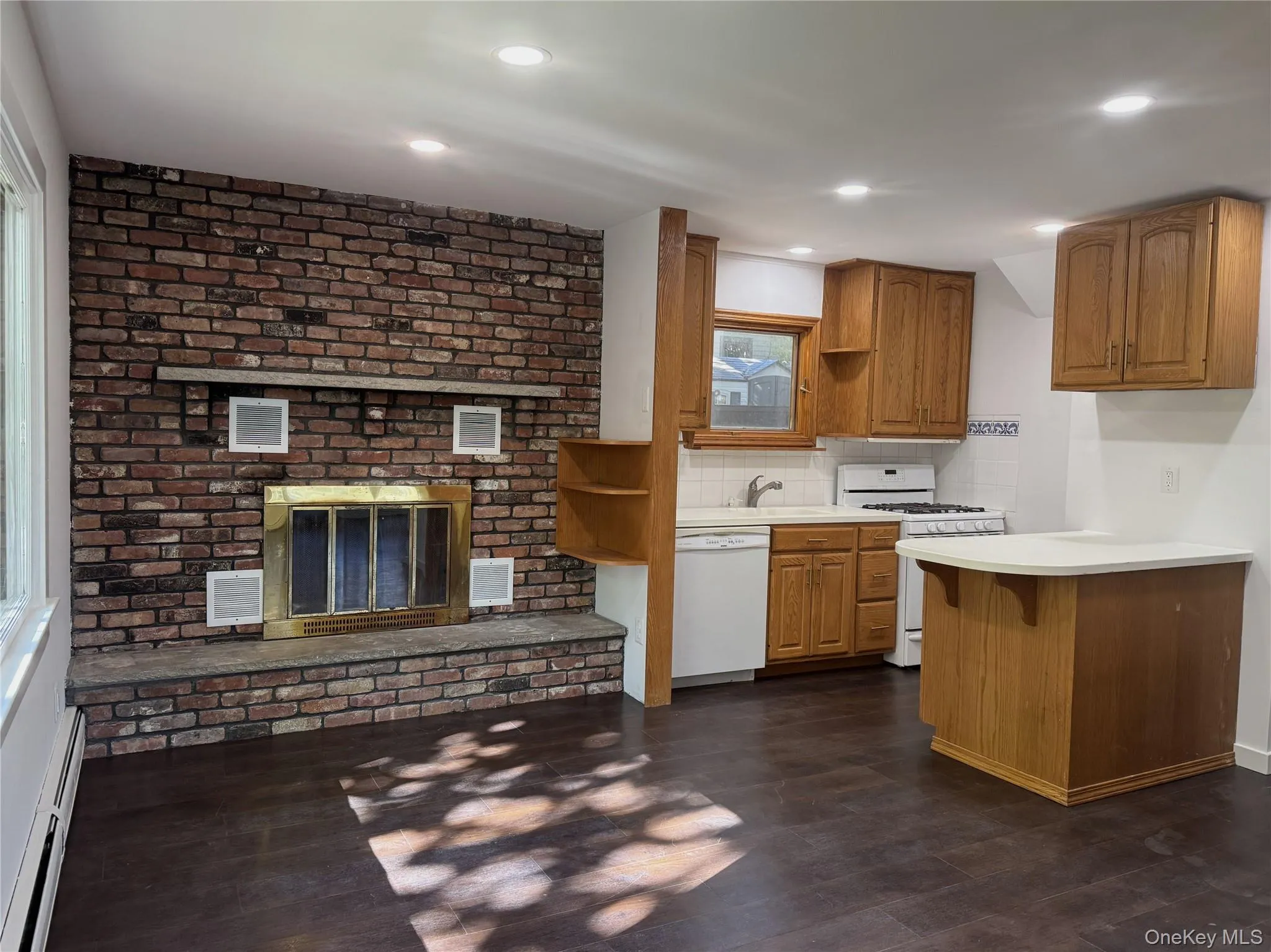 Kitchen with light countertops, brown cabinetry, baseboard heating, white appliances, and tasteful backsplash Kitchen with light countertops, brown cabinetry, baseboard heating, white appliances, and tasteful backsplash