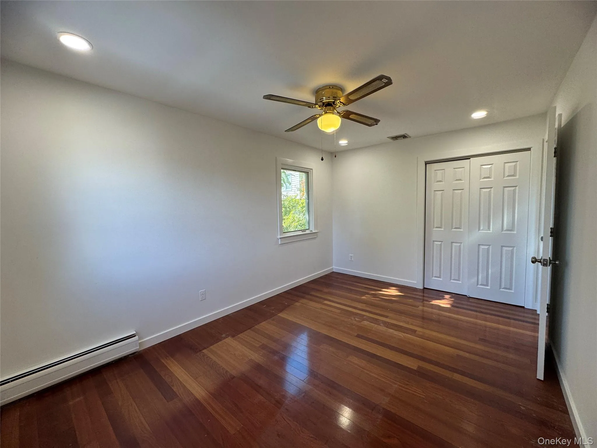 Unfurnished bedroom with recessed lighting, a baseboard heating unit, dark wood-style flooring, a ceiling fan, and a closet Unfurnished bedroom with recessed lighting, a baseboard heating unit, dark wood-style flooring, a ceiling fan, and a closet