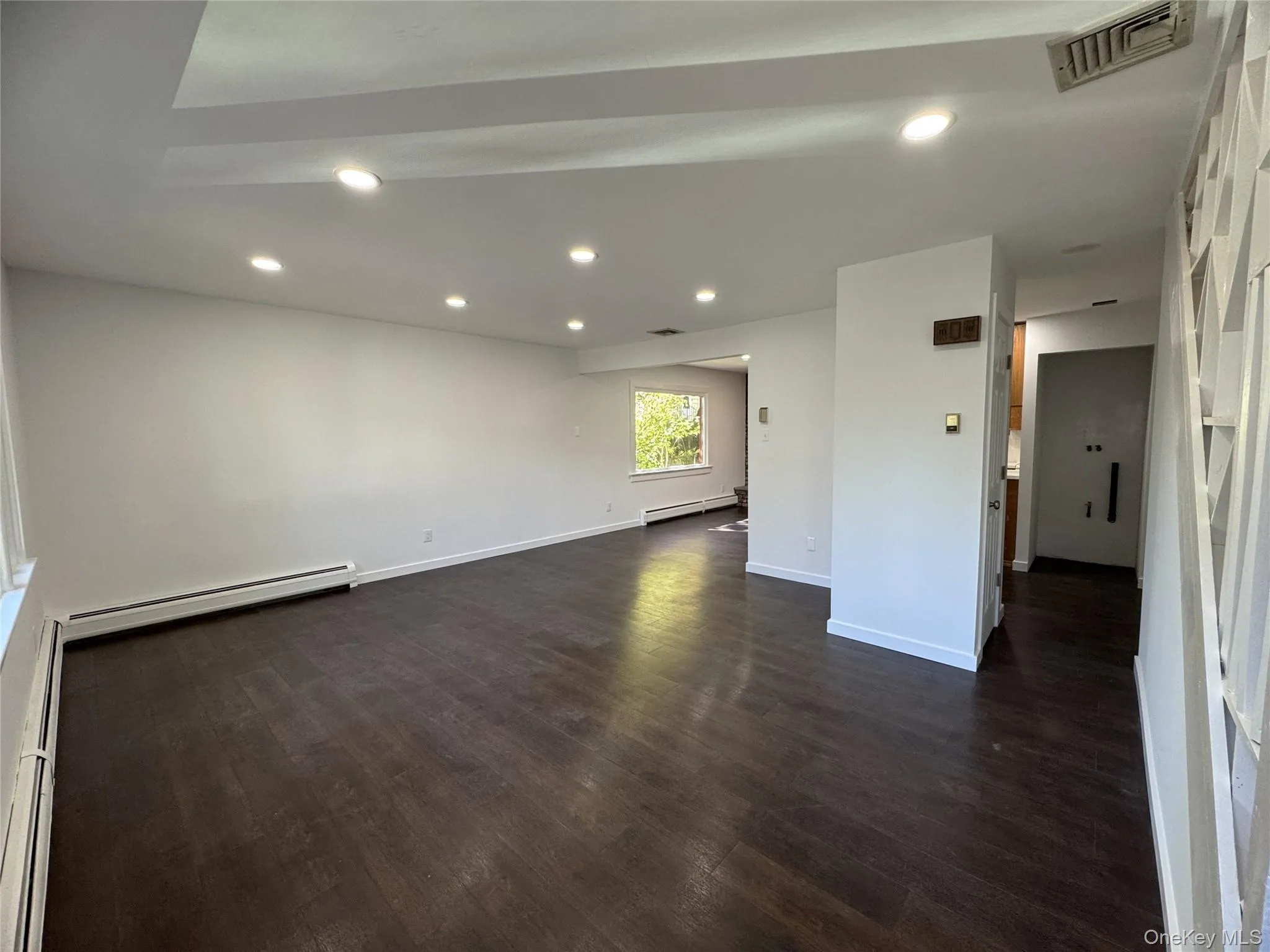 Unfurnished living room with recessed lighting, a baseboard heating unit, and dark wood-type flooring Unfurnished living room with recessed lighting, a baseboard heating unit, and dark wood-type flooring