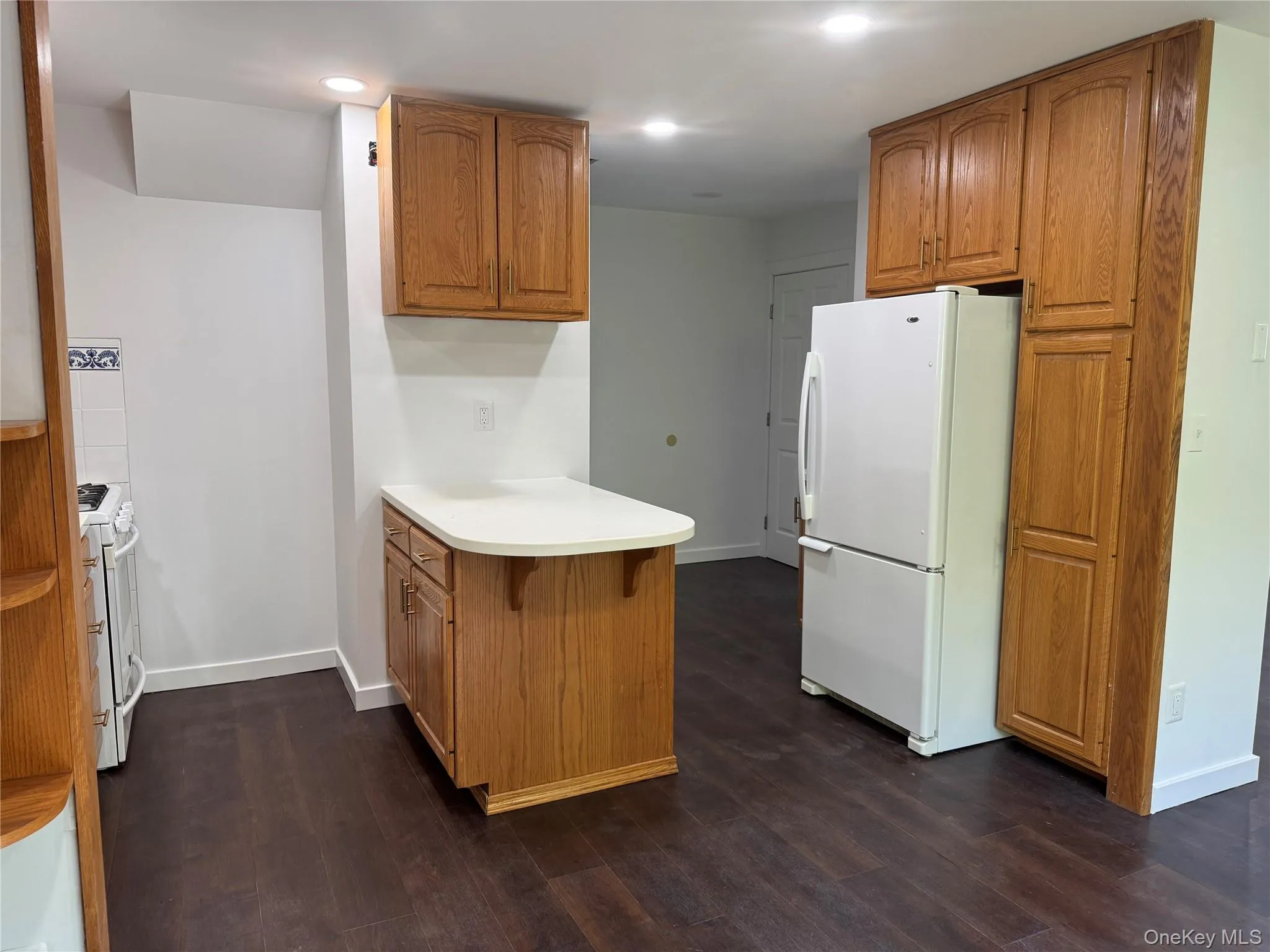 Kitchen with brown cabinets, a peninsula, white appliances, light countertops, and dark wood-type flooring Kitchen with brown cabinets, a peninsula, white appliances, light countertops, and dark wood-type flooring