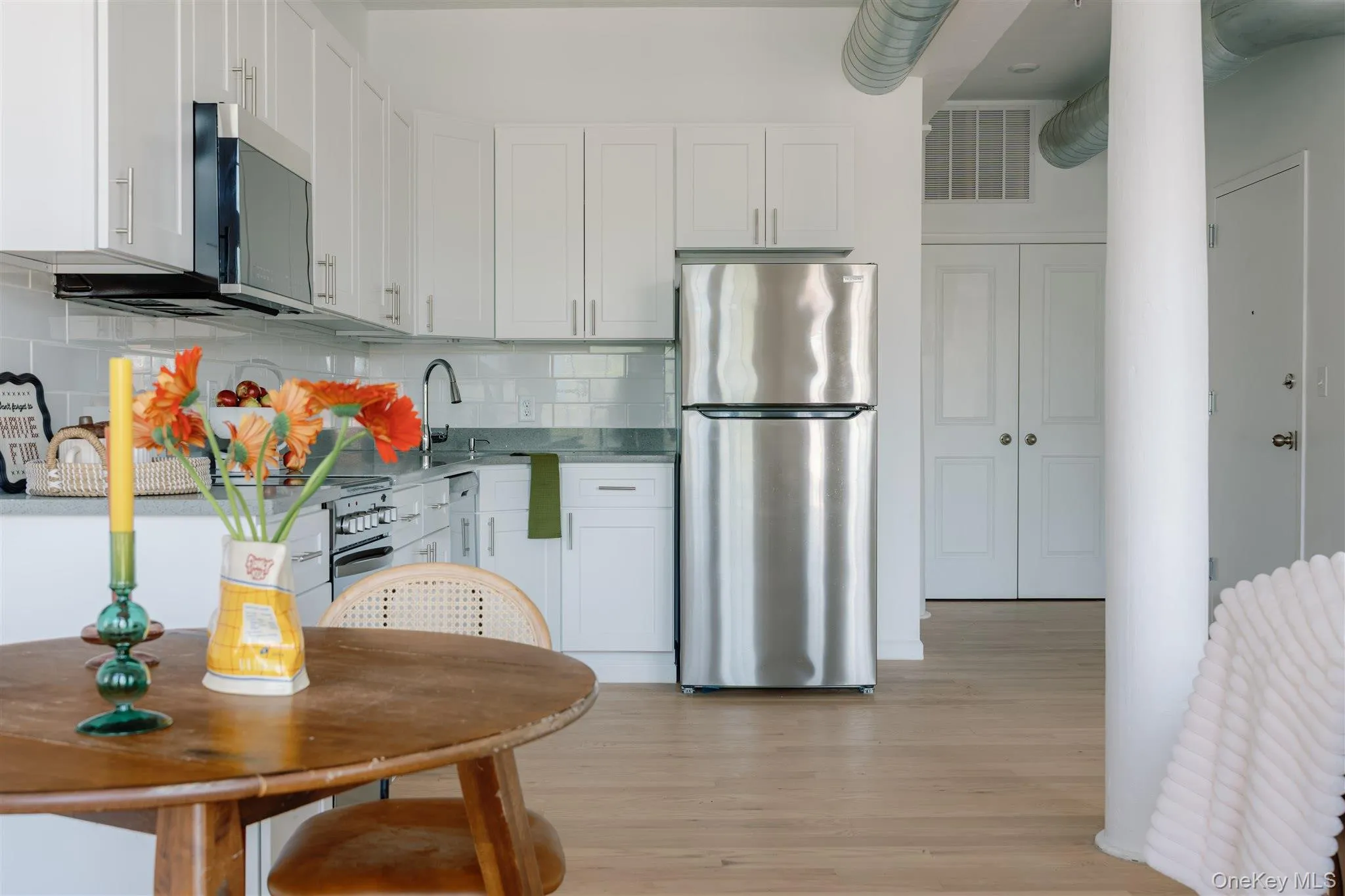 Kitchen with stainless steel appliances, white cabinets, light wood-style floors, decorative backsplash, and light stone counters Kitchen with stainless steel appliances, white cabinets, light wood-style floors, decorative backsplash, and light stone counters