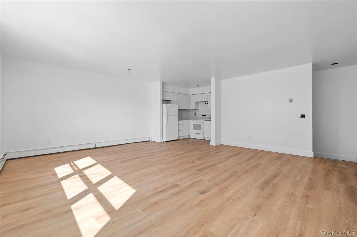 Unfurnished living room featuring light wood-type flooring and a baseboard heating unit Unfurnished living room featuring light wood-type flooring and a baseboard heating unit