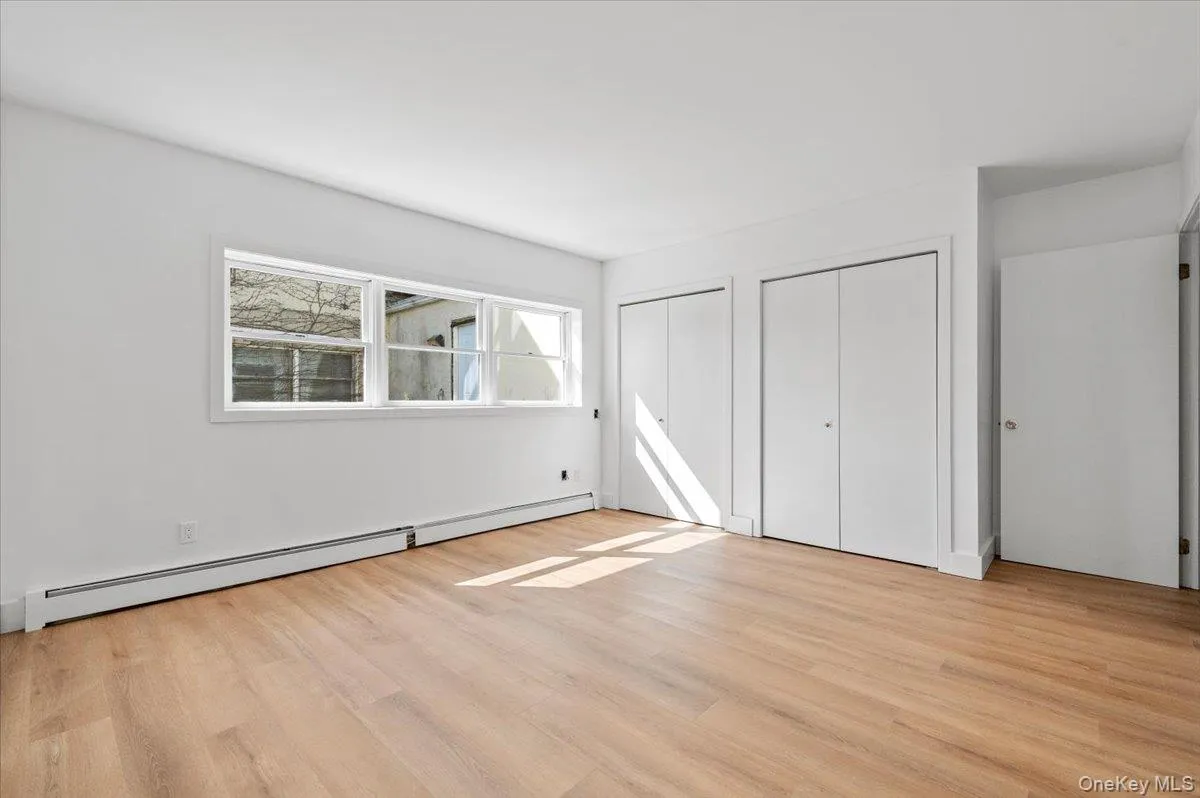 Unfurnished bedroom featuring a baseboard radiator, multiple closets, and light wood finished floors Unfurnished bedroom featuring a baseboard radiator, multiple closets, and light wood finished floors