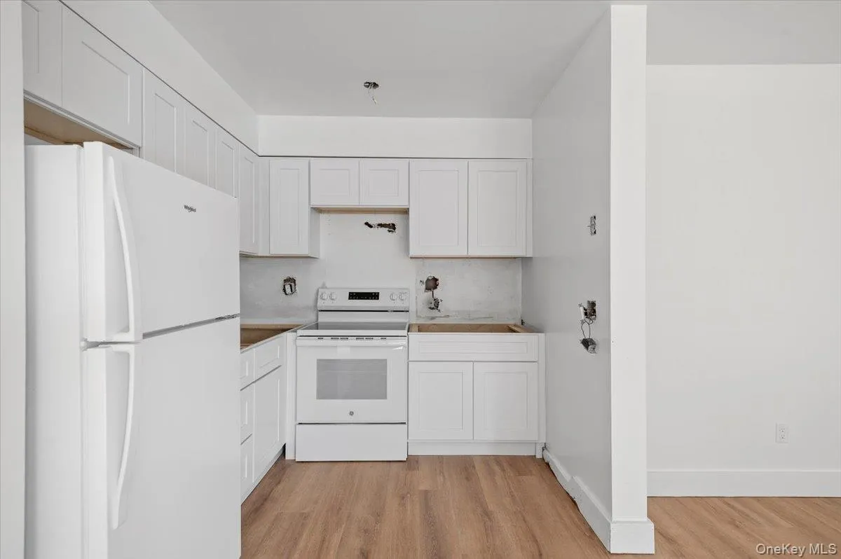 Kitchen with white appliances, white cabinetry, and light wood-style flooring Kitchen with white appliances, white cabinetry, and light wood-style flooring