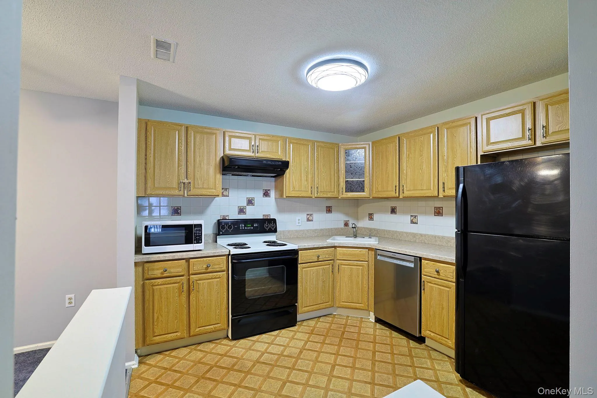 Kitchen featuring black appliances, light countertops, under cabinet range hood, decorative backsplash, and light floors Kitchen featuring black appliances, light countertops, under cabinet range hood, decorative backsplash, and light floors