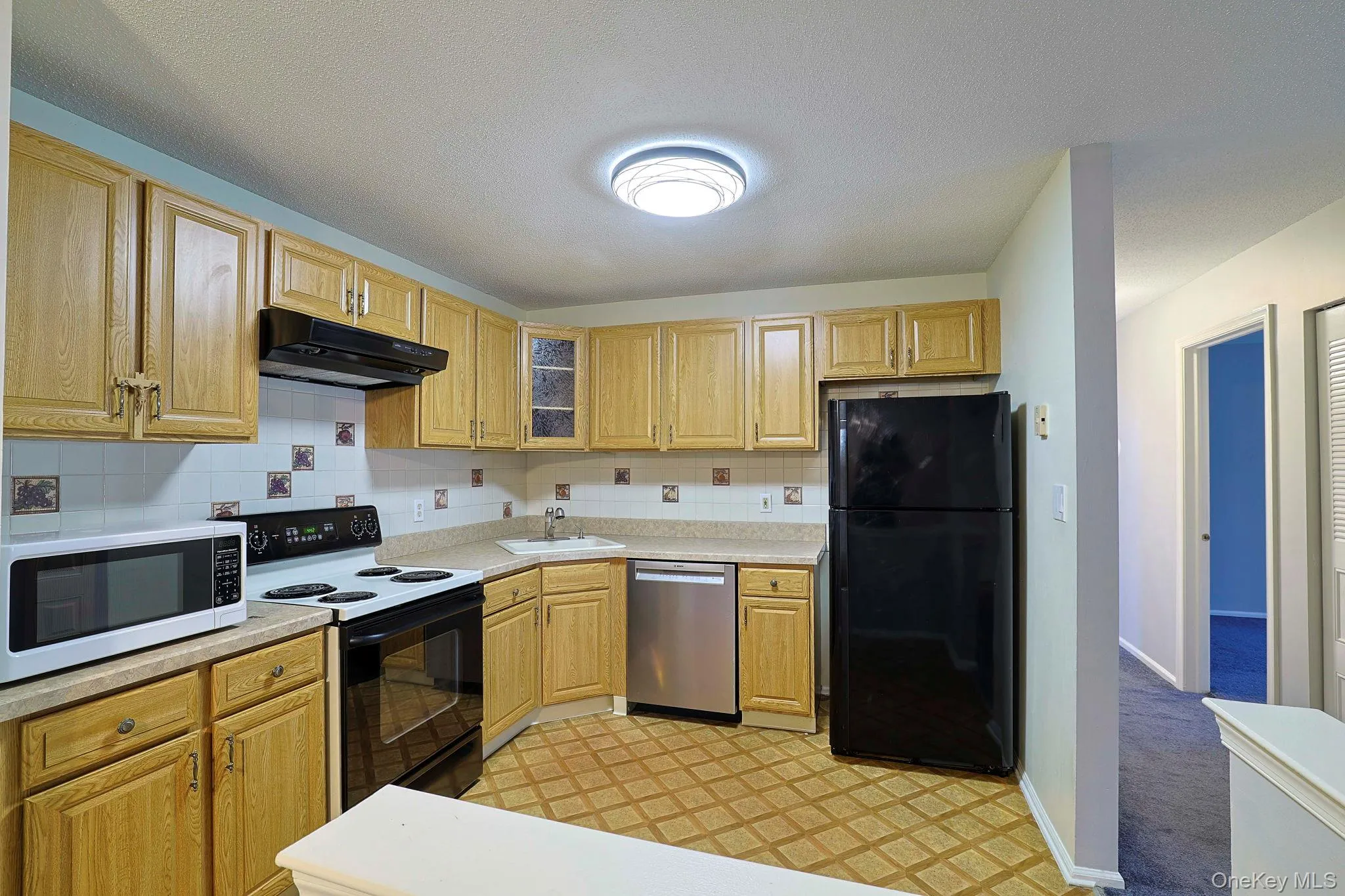 Kitchen featuring range with electric cooktop, white microwave, freestanding refrigerator, and backsplash Kitchen featuring range with electric cooktop, white microwave, freestanding refrigerator, and backsplash