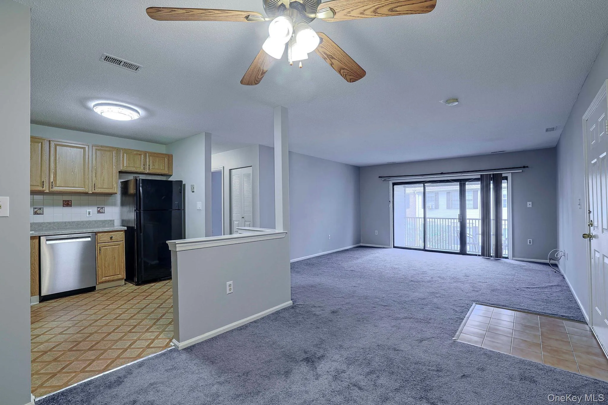 Kitchen featuring light colored carpet, freestanding refrigerator, stainless steel dishwasher, a ceiling fan, and light countertops Kitchen featuring light colored carpet, freestanding refrigerator, stainless steel dishwasher, a ceiling fan, and light countertops