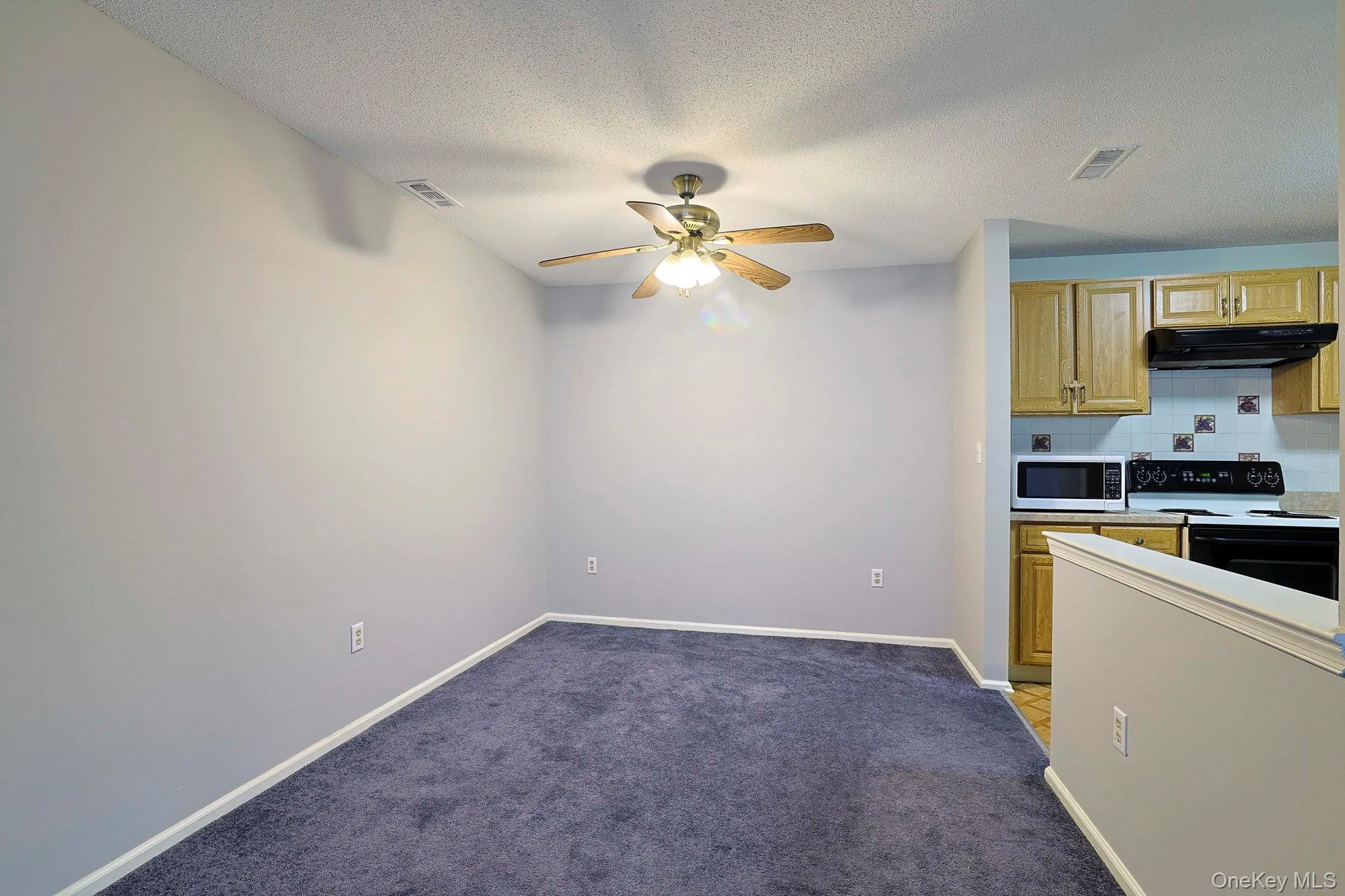 Kitchen with backsplash, electric stove, light colored carpet, light countertops, and a textured ceiling Kitchen with backsplash, electric stove, light colored carpet, light countertops, and a textured ceiling