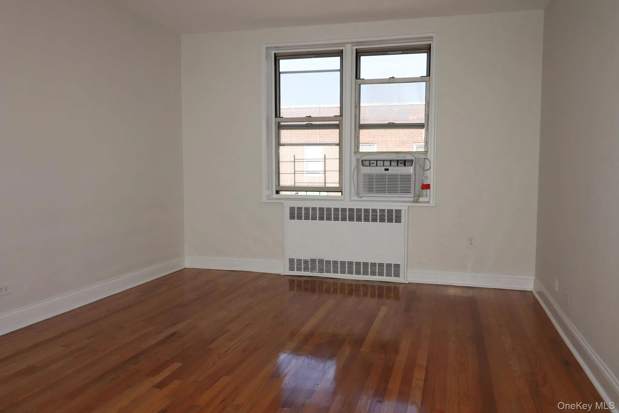 Empty room featuring radiator heating unit, dark wood finished floors, and cooling unit Empty room featuring radiator heating unit, dark wood finished floors, and cooling unit