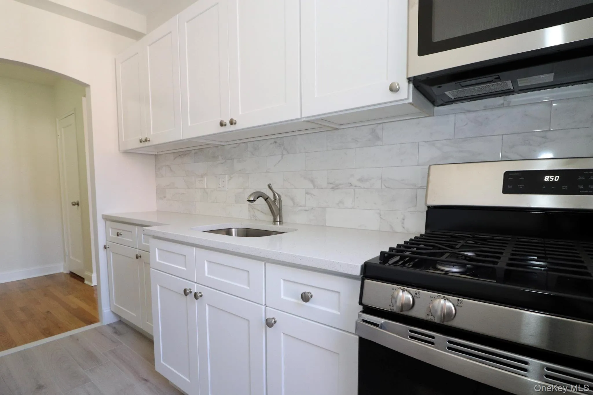 Kitchen featuring appliances with stainless steel finishes, white cabinetry, light wood finished floors, light stone counters, and backsplash Kitchen featuring appliances with stainless steel finishes, white cabinetry, light wood finished floors, light stone counters, and backsplash