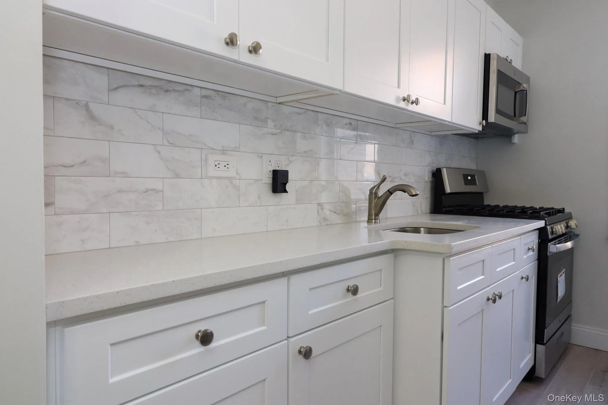 Kitchen featuring appliances with stainless steel finishes, white cabinets, light stone counters, backsplash, and dark wood-style floors Kitchen featuring appliances with stainless steel finishes, white cabinets, light stone counters, backsplash, and dark wood-style floors