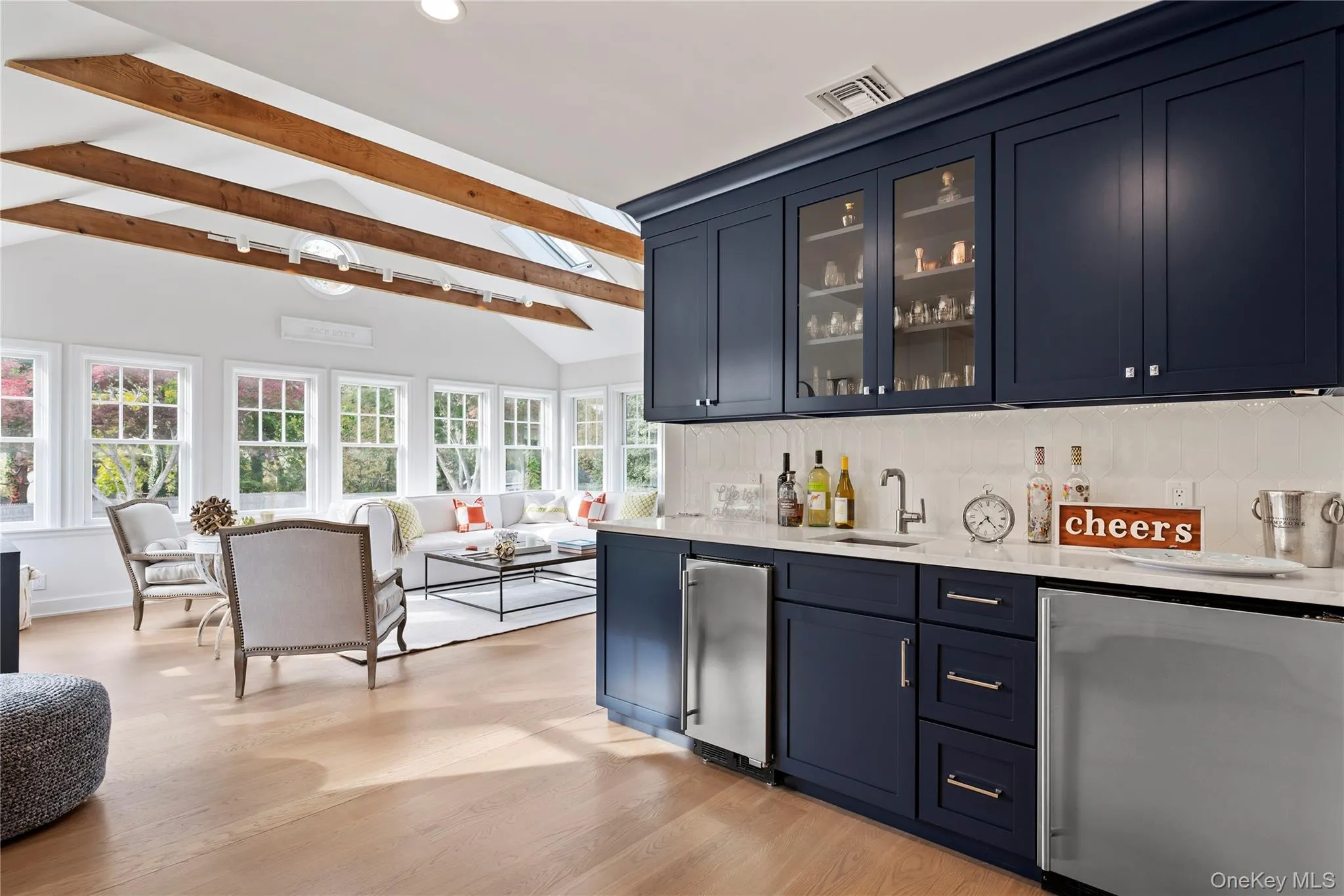 Indoor wet bar with stainless steel fridge, decorative backsplash, blue cabinets, light stone counters, and glass insert cabinets