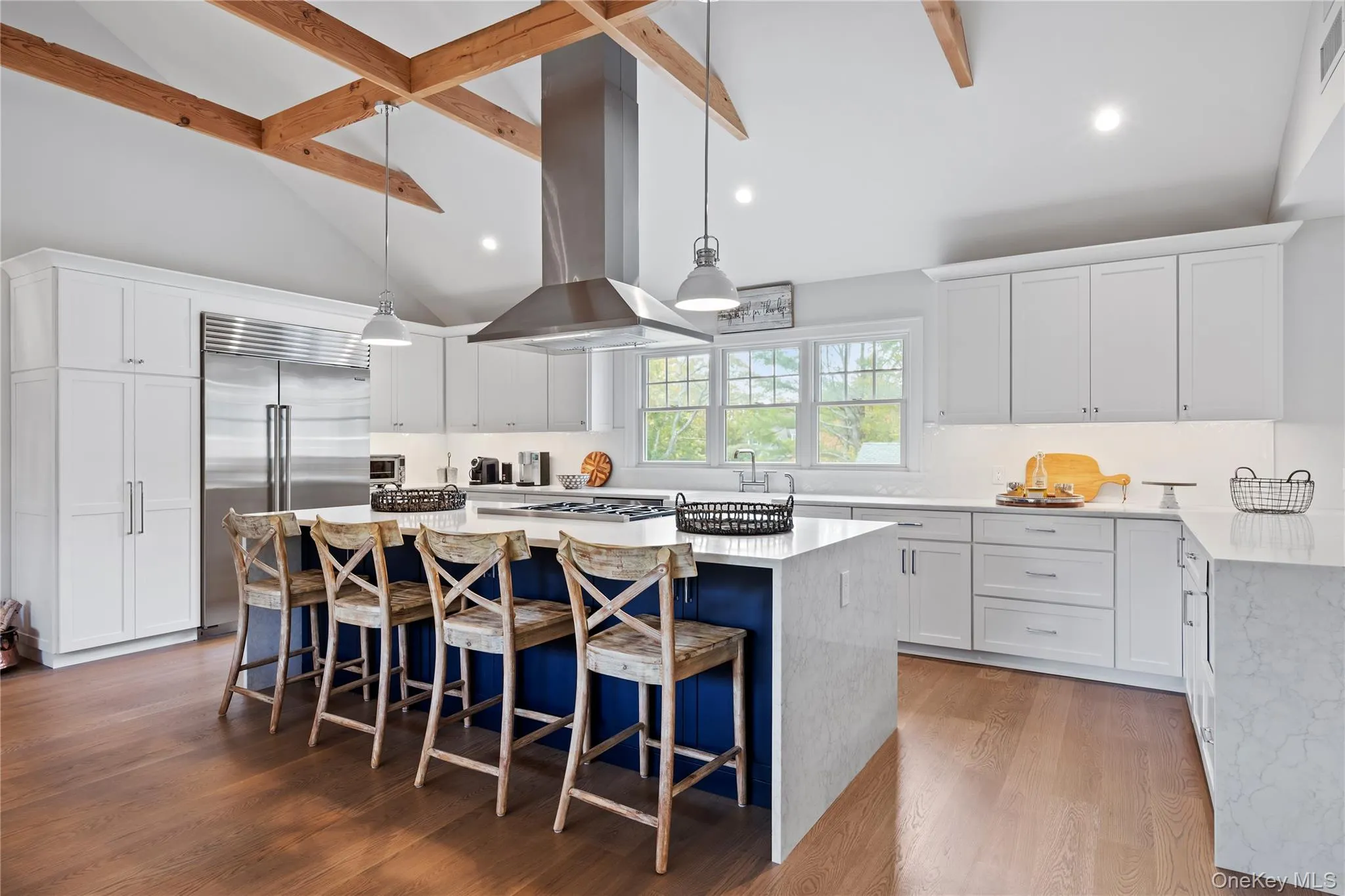 Kitchen with white cabinets, light stone counters, beam ceiling, hanging light fixtures, and a breakfast bar