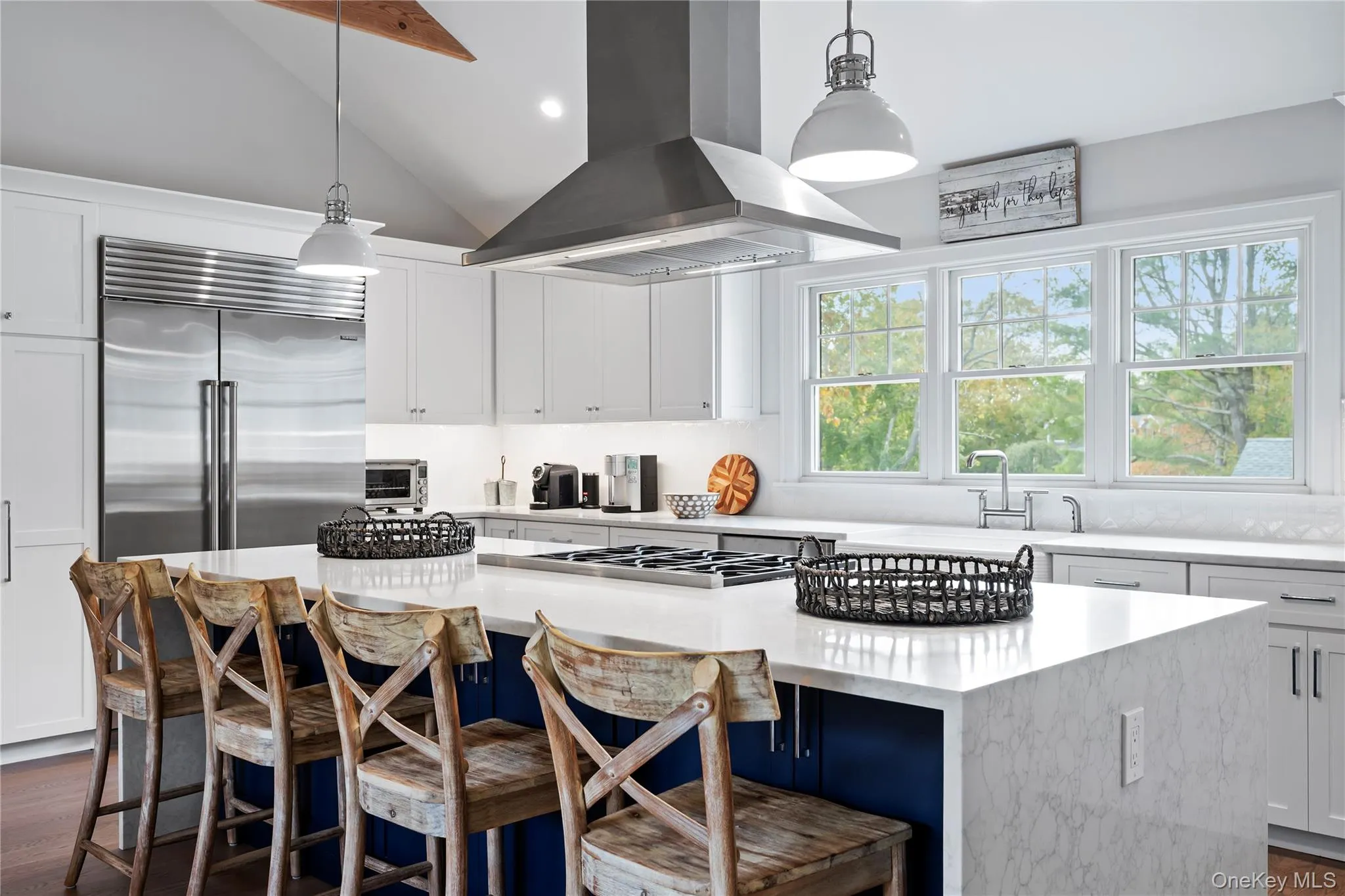 Kitchen featuring white cabinetry, island exhaust hood, vaulted ceiling, a breakfast bar, and pendant lighting