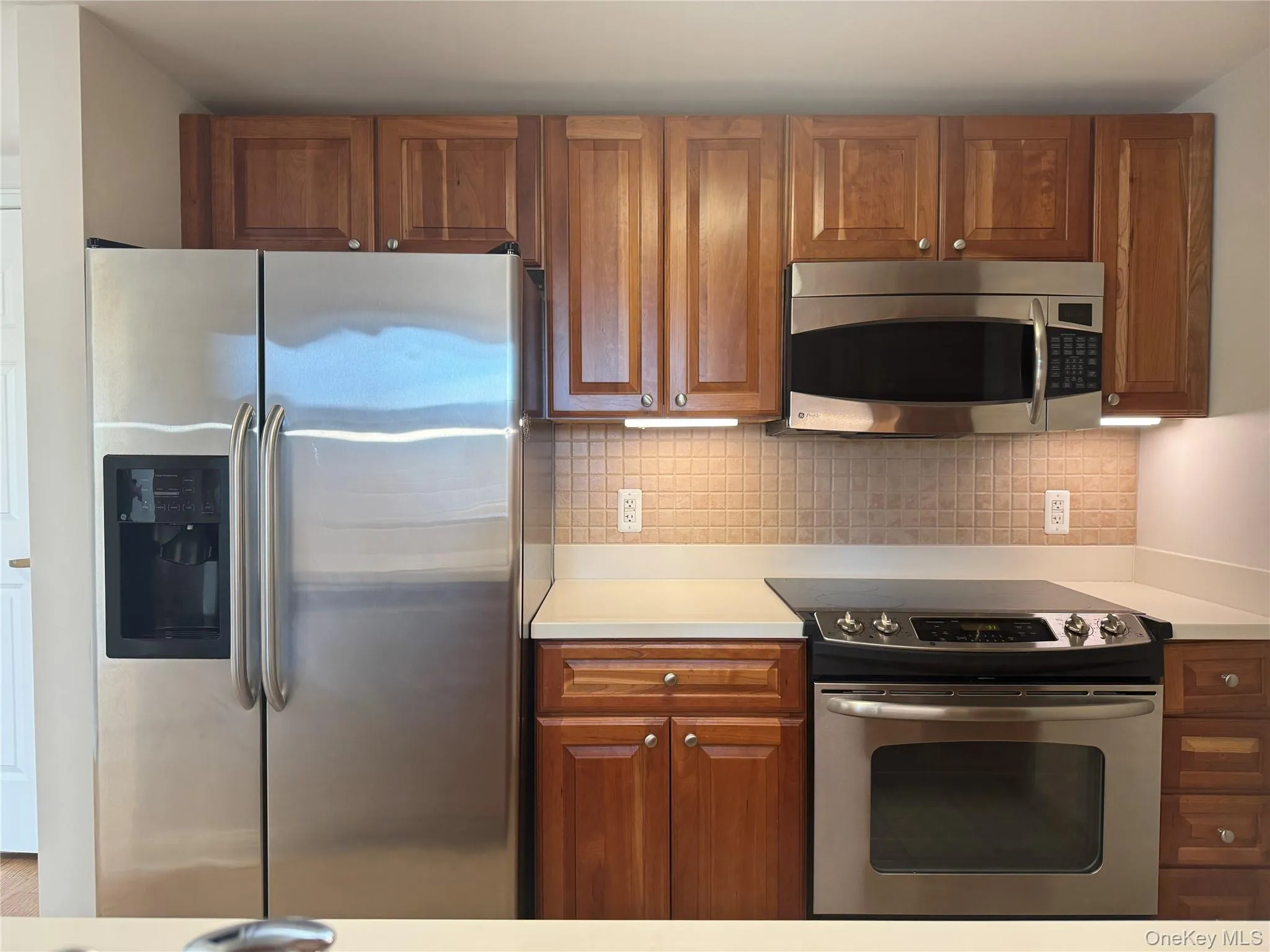 Kitchen featuring stainless steel appliances, light countertops, brown cabinetry, and tasteful backsplash Kitchen featuring stainless steel appliances, light countertops, brown cabinetry, and tasteful backsplash