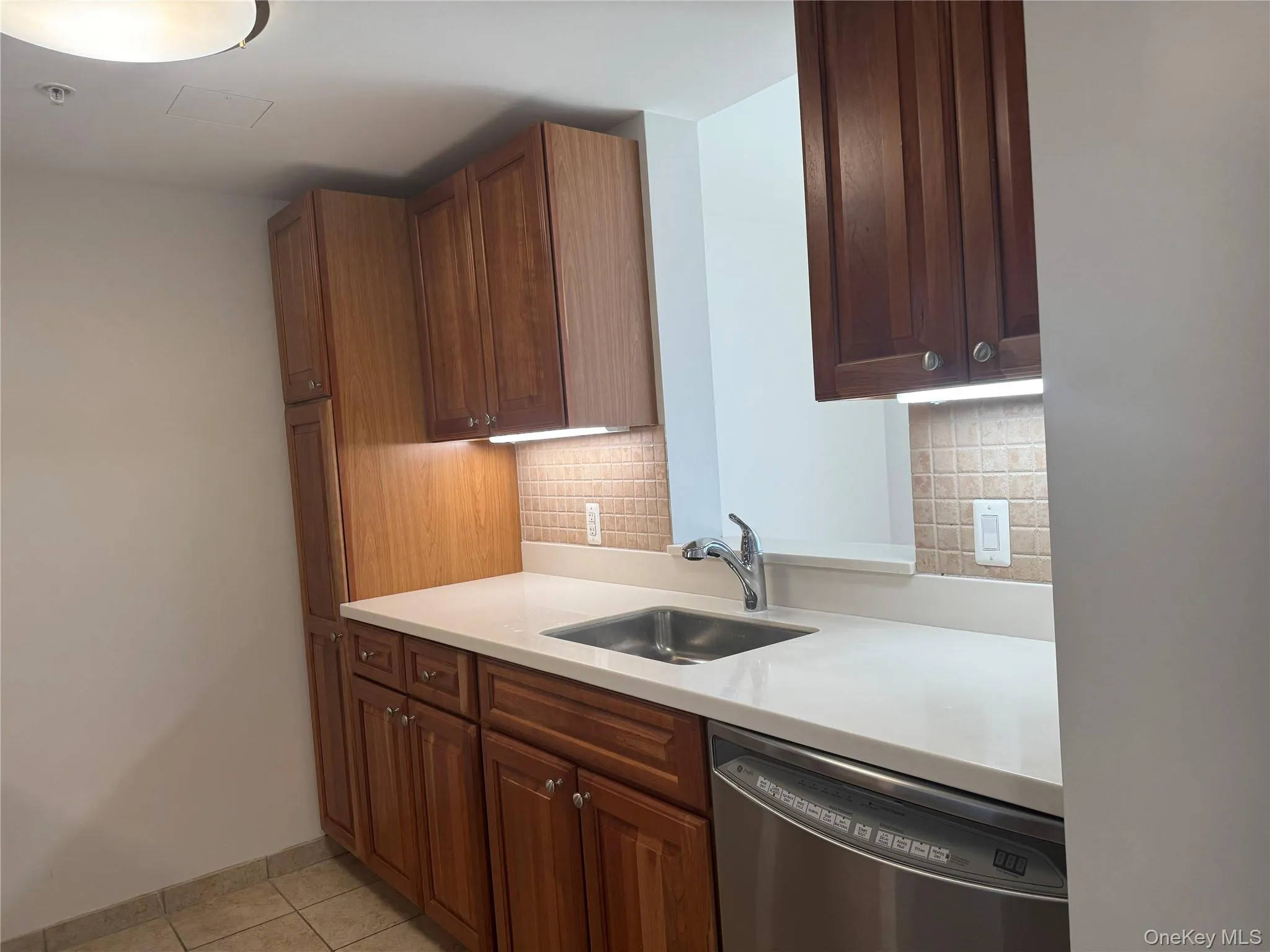 Kitchen featuring dishwasher, tasteful backsplash, light tile patterned floors, and brown cabinets Kitchen featuring dishwasher, tasteful backsplash, light tile patterned floors, and brown cabinets
