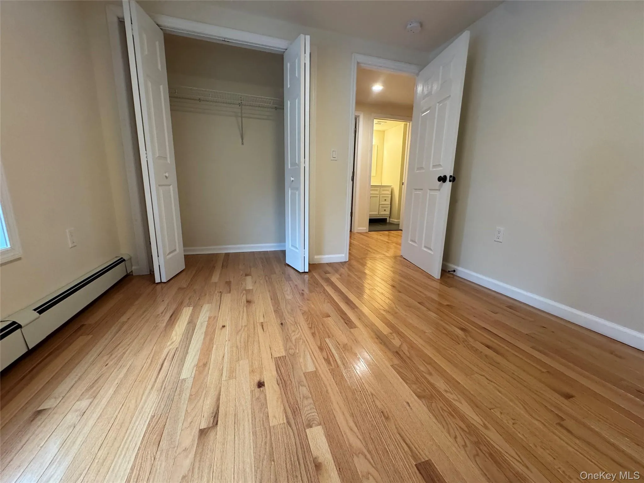 Unfurnished bedroom featuring light wood-style flooring, a closet, and a baseboard heating unit Unfurnished bedroom featuring light wood-style flooring, a closet, and a baseboard heating unit