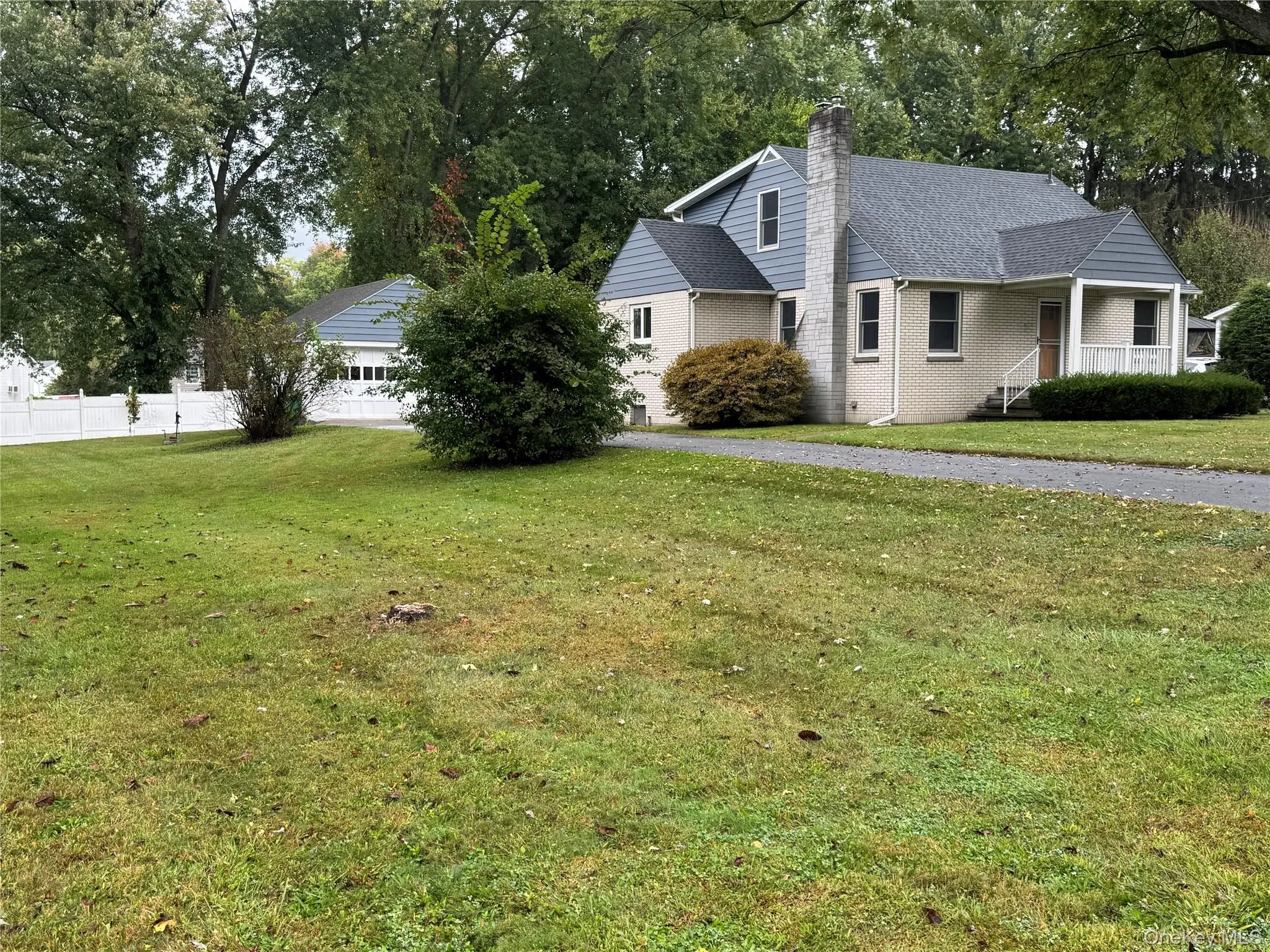 View of front of property featuring covered porch, a chimney, brick siding, a shingled roof, and view of wooded area View of front of property featuring covered porch, a chimney, brick siding, a shingled roof, and view of wooded area