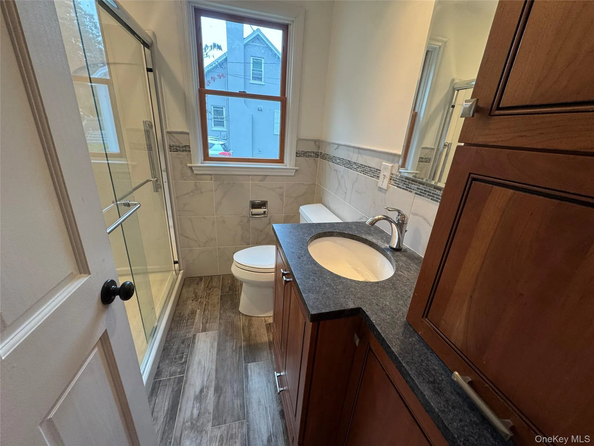 Bathroom featuring dark wood-style flooring, a stall shower, vanity, tile walls, and wainscoting Bathroom featuring dark wood-style flooring, a stall shower, vanity, tile walls, and wainscoting