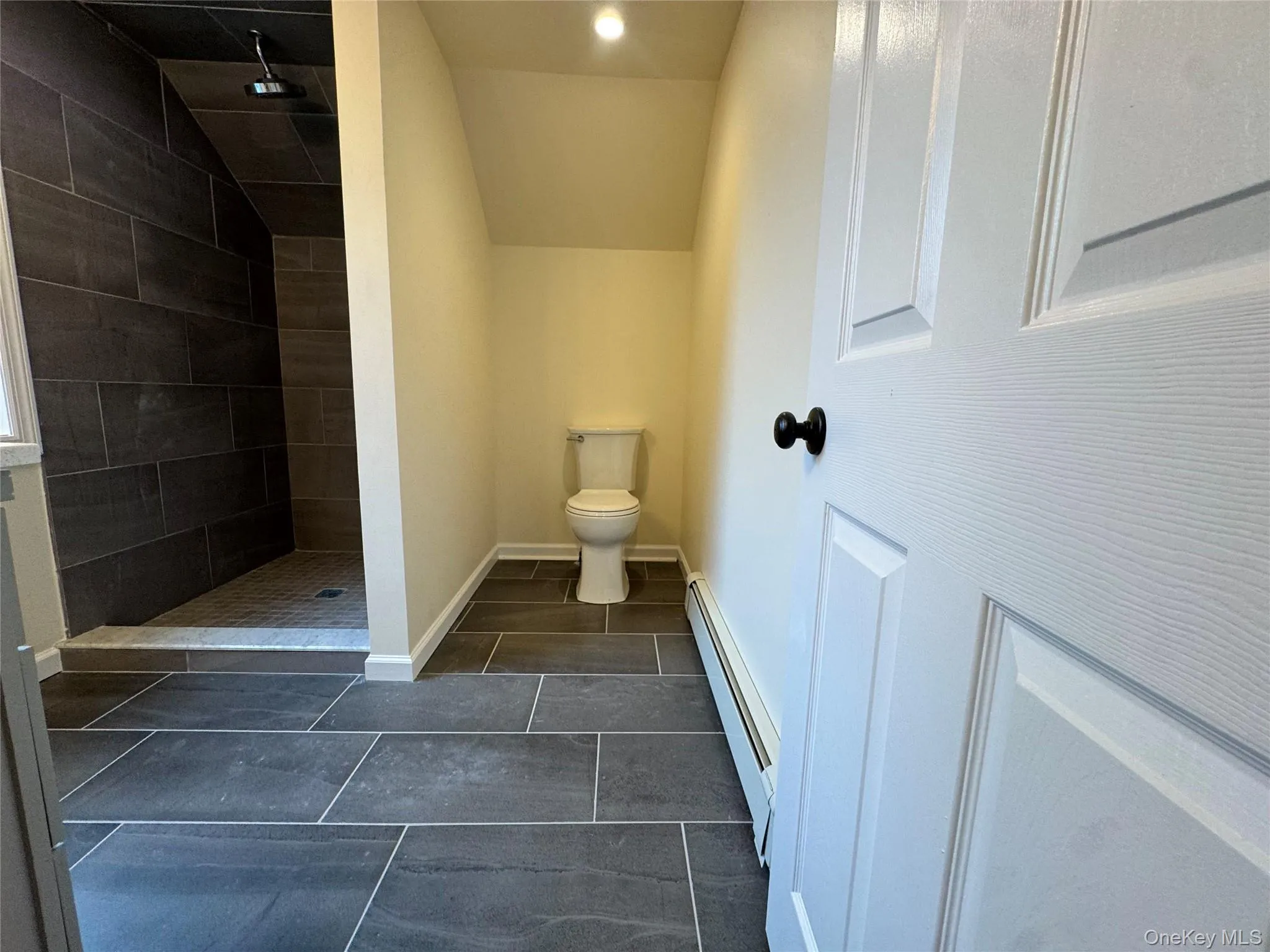 Bathroom featuring a stall shower, a baseboard radiator, lofted ceiling, dark tile patterned floors, and recessed lighting Bathroom featuring a stall shower, a baseboard radiator, lofted ceiling, dark tile patterned floors, and recessed lighting
